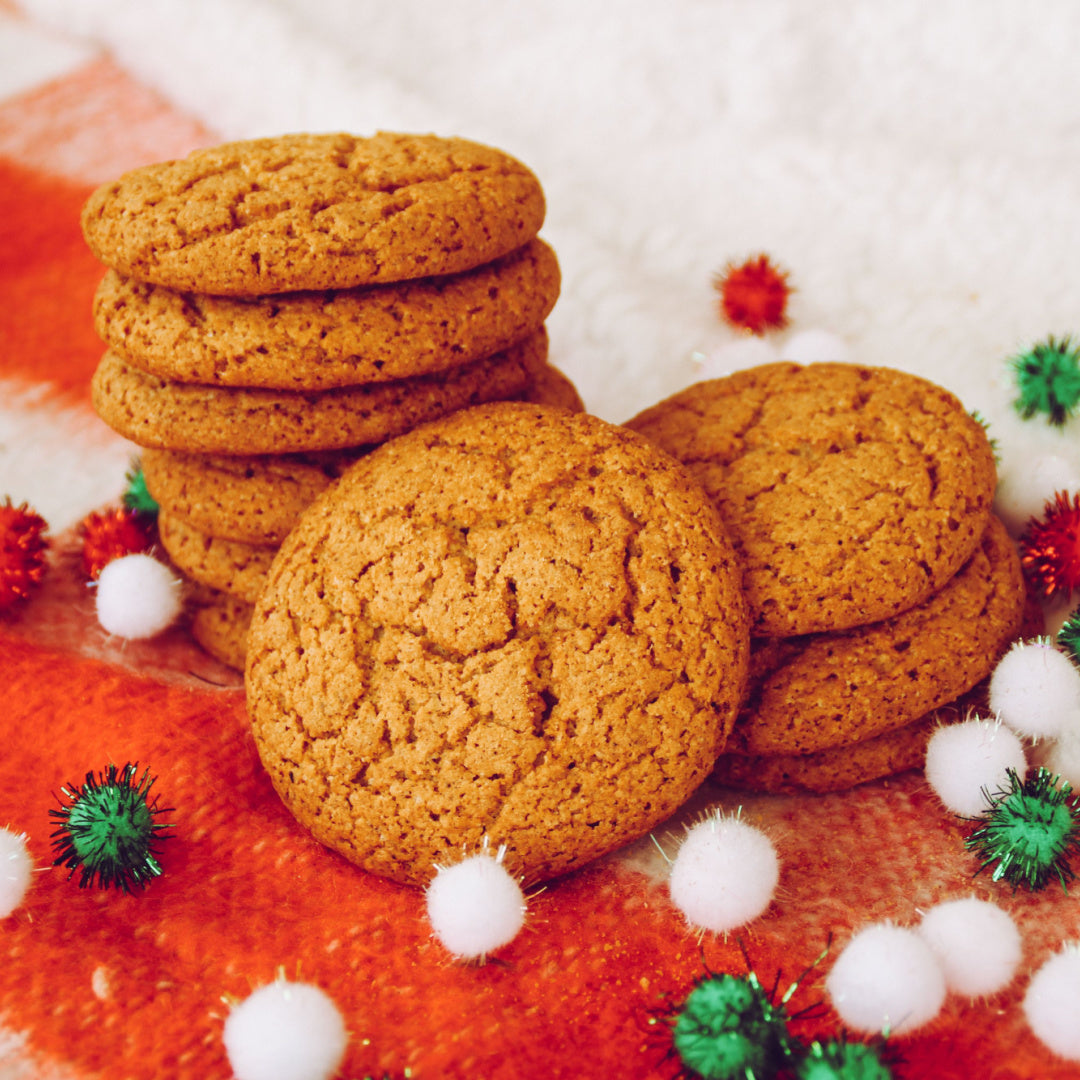 A stack of fresh gingersnap cookies rest on a holiday backdrop. These cookies are the inspiration for our Christmas candle of the same name.