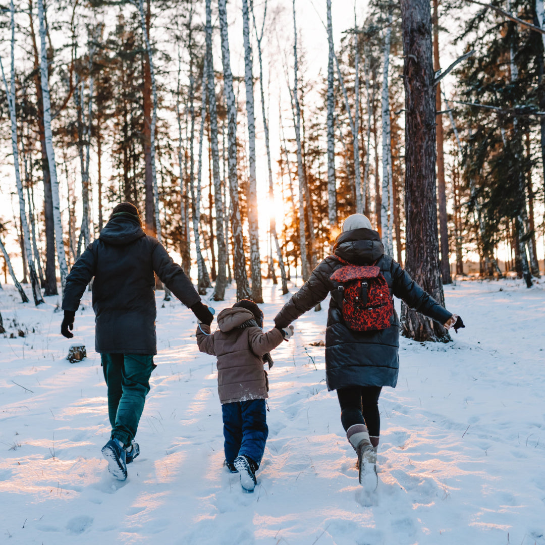 A family walks through a winter forest at sunset. This sensation is the inspiration behind our "Winter Woods" scented candle