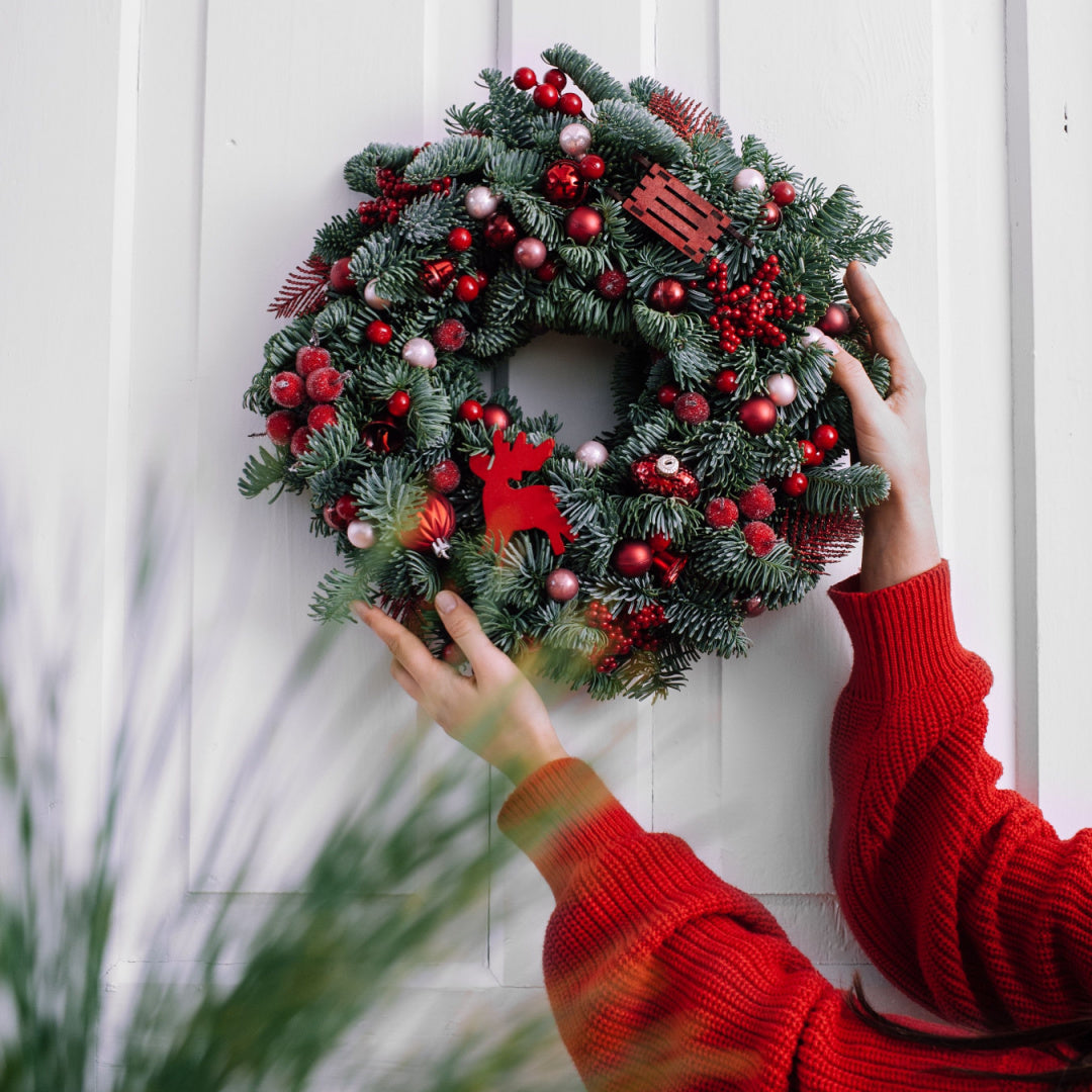 A photo of a christmas wreath being hung on a front door. This image is the inspiration for our "Balsam Wreath" Christmas scented candle
