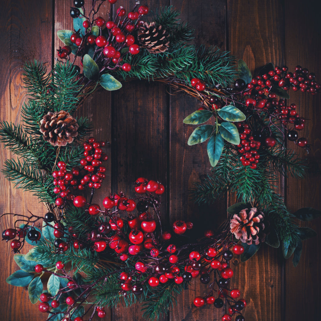 A wreat of holly berried laid out on a dark wood table.