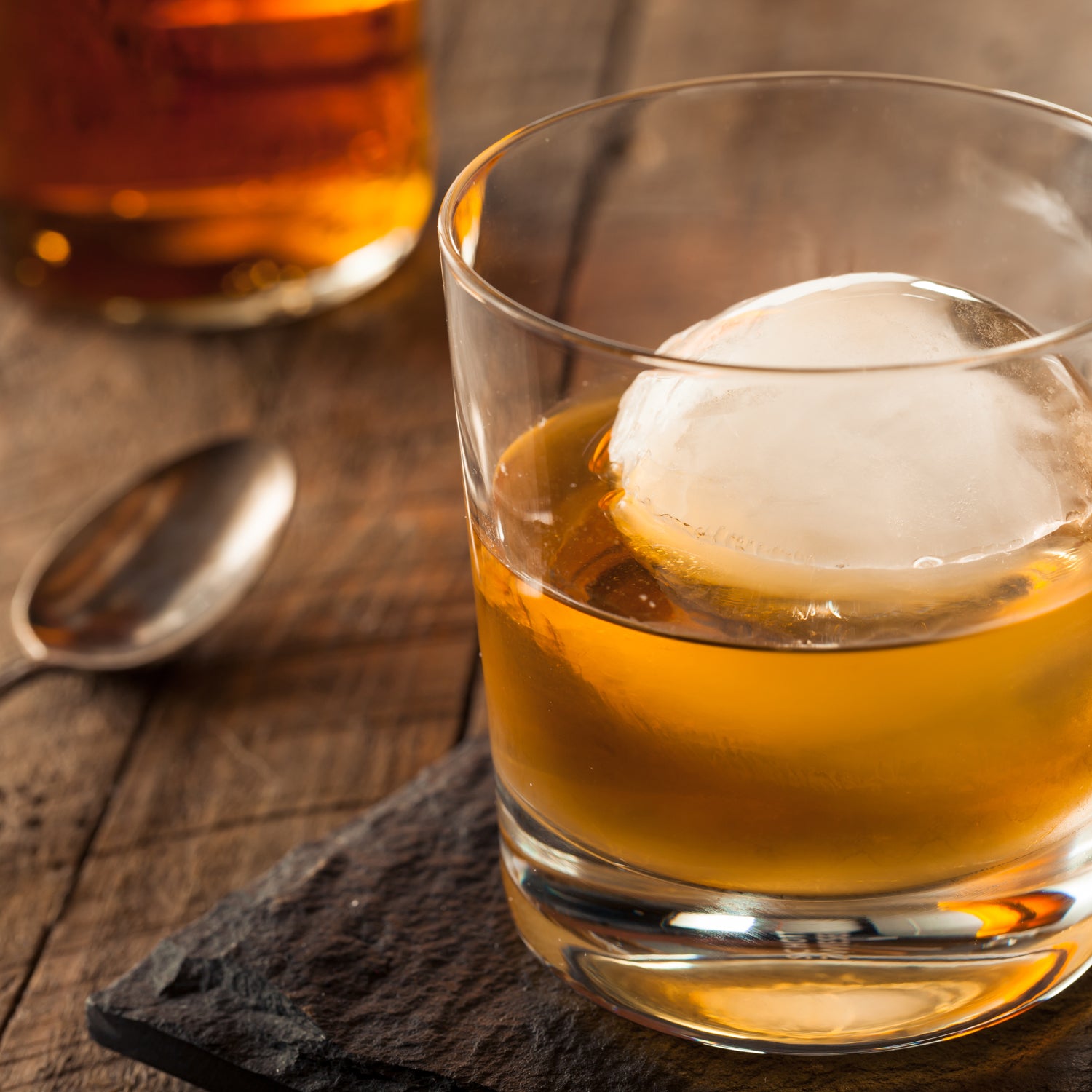 A glass of Tuscany Candle® EVD Maple Bourbon Scented Jar Candle (12 oz) – Farmhouse Collection with an ice cube in it, exuding a rustic candle ambiance.