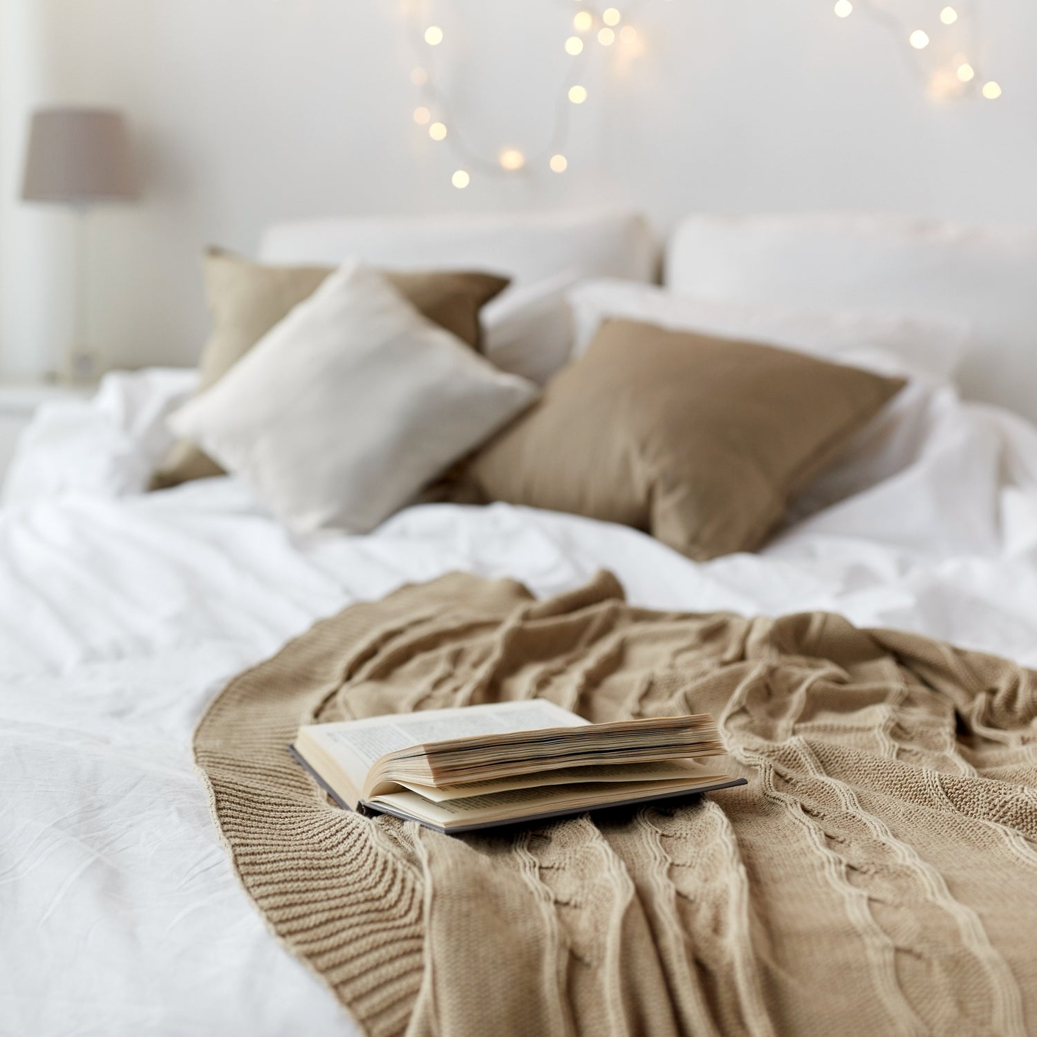 A cozy bed with a soft blanket and a Comforts of Home Scented Jar Candle (12 oz) – Farmhouse Collection by Tuscany Candle® EVD on it.