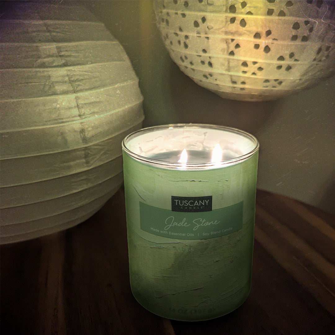 A Jade Stone Scented Jar Candle (14 oz) – part of our Home Décor Collection by Tuscany Candle – is peacefully sitting on a table adorned with elegant paper lanterns. Infused with calming essential oils, this candle adds both aesthetic charm.