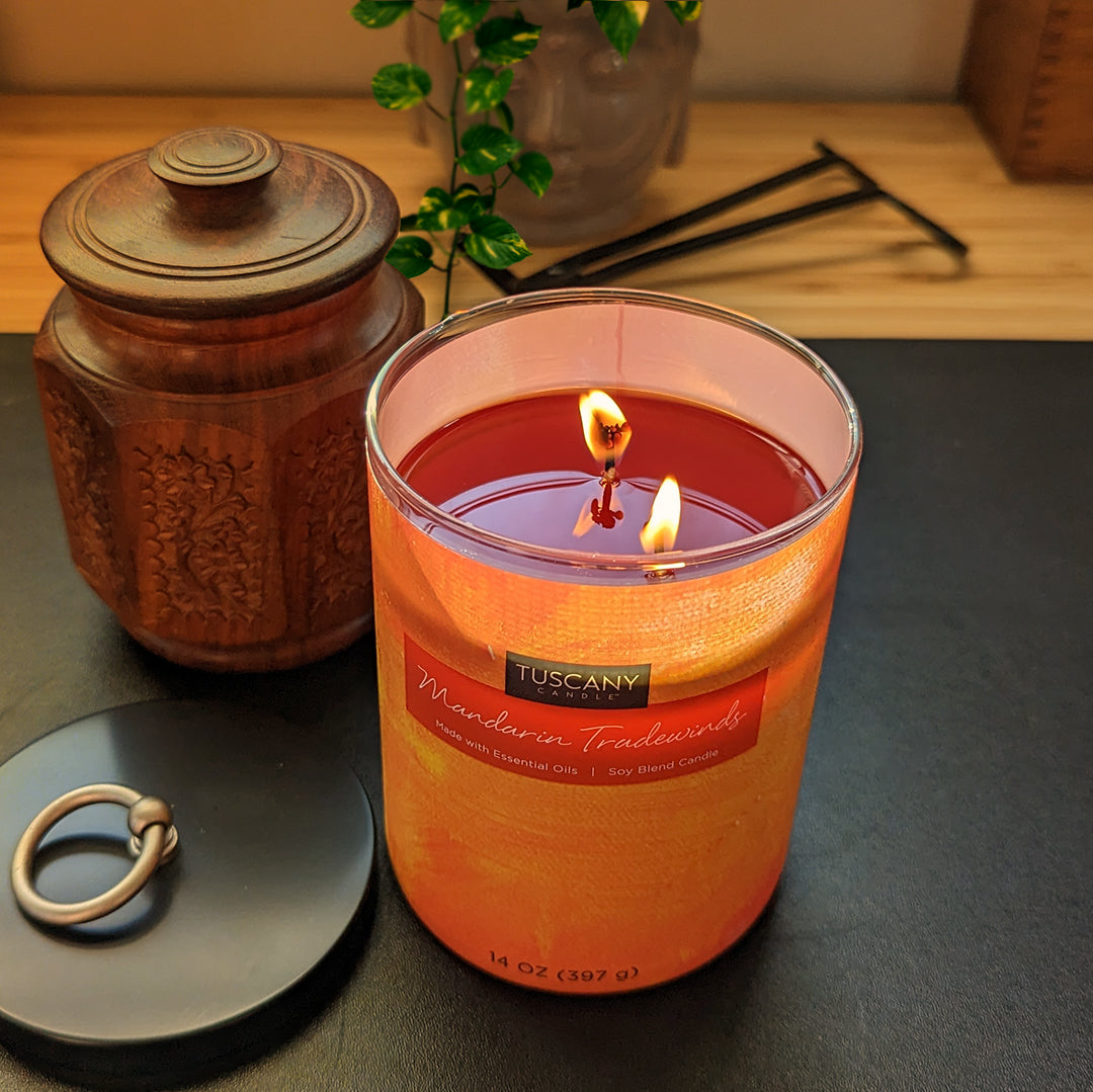 A Mandarin Tradewinds scented jar candle (14 oz) from the Tuscany Candle Home Décor Collection, on a table next to a ring, providing an inviting ambiance and perfect for enhancing your home décor.