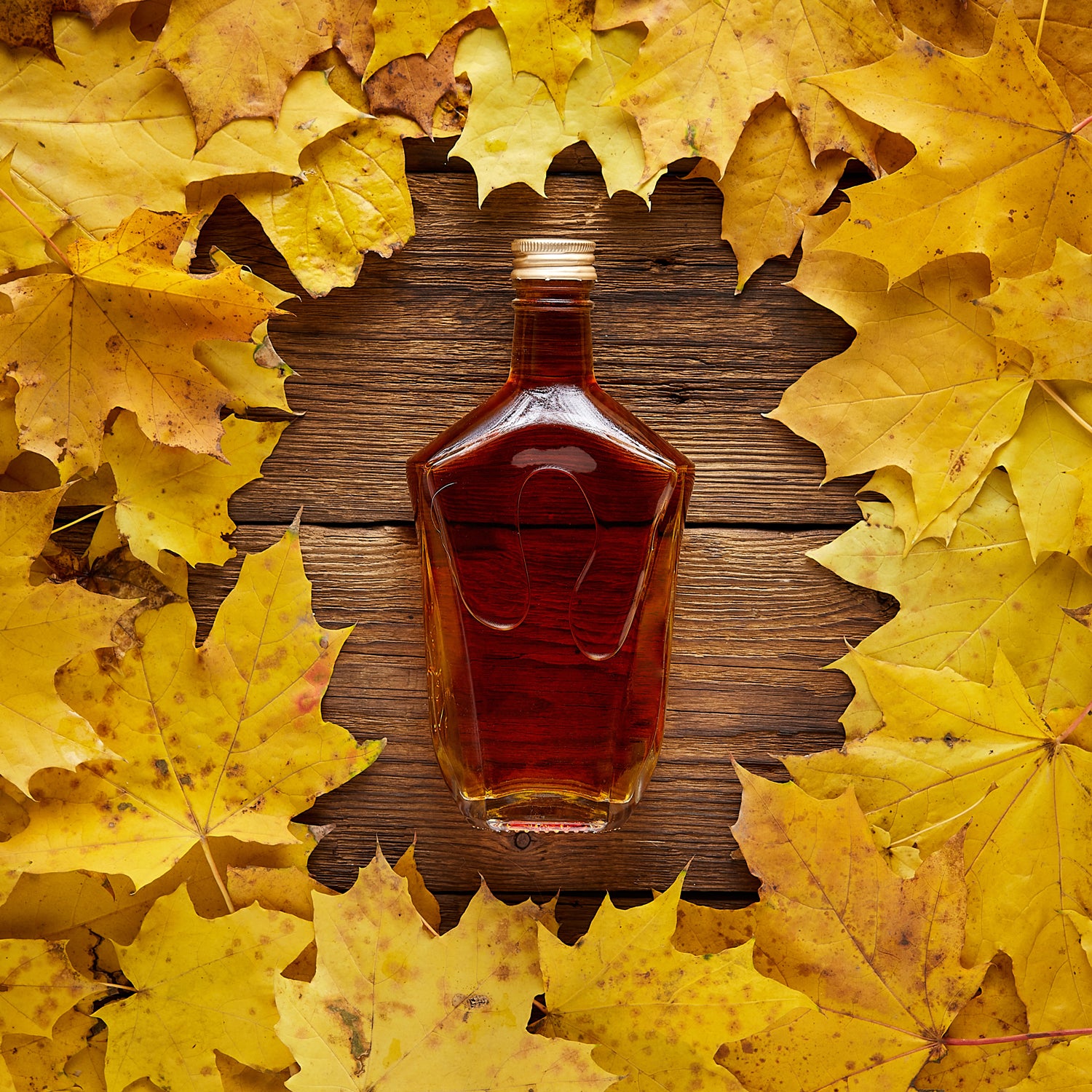 A Maple Bourbon Scented Jar Candle (12 oz) – Farmhouse Collection by Tuscany Candle surrounded by autumn leaves, creating a farmhouse ambiance.