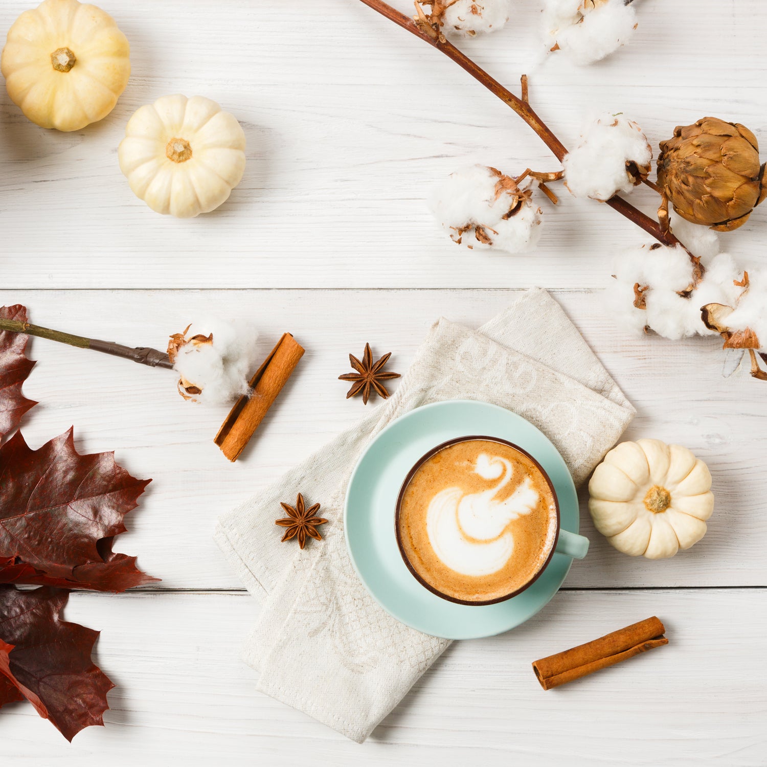 A cup of coffee with Spiced Pumpkin Long-Lasting Scented Jar Candle (14 oz) by Tuscany Candle on a white wooden table. The warm fragrance notes of cinnamon fill the air, enhancing the cozy ambiance.