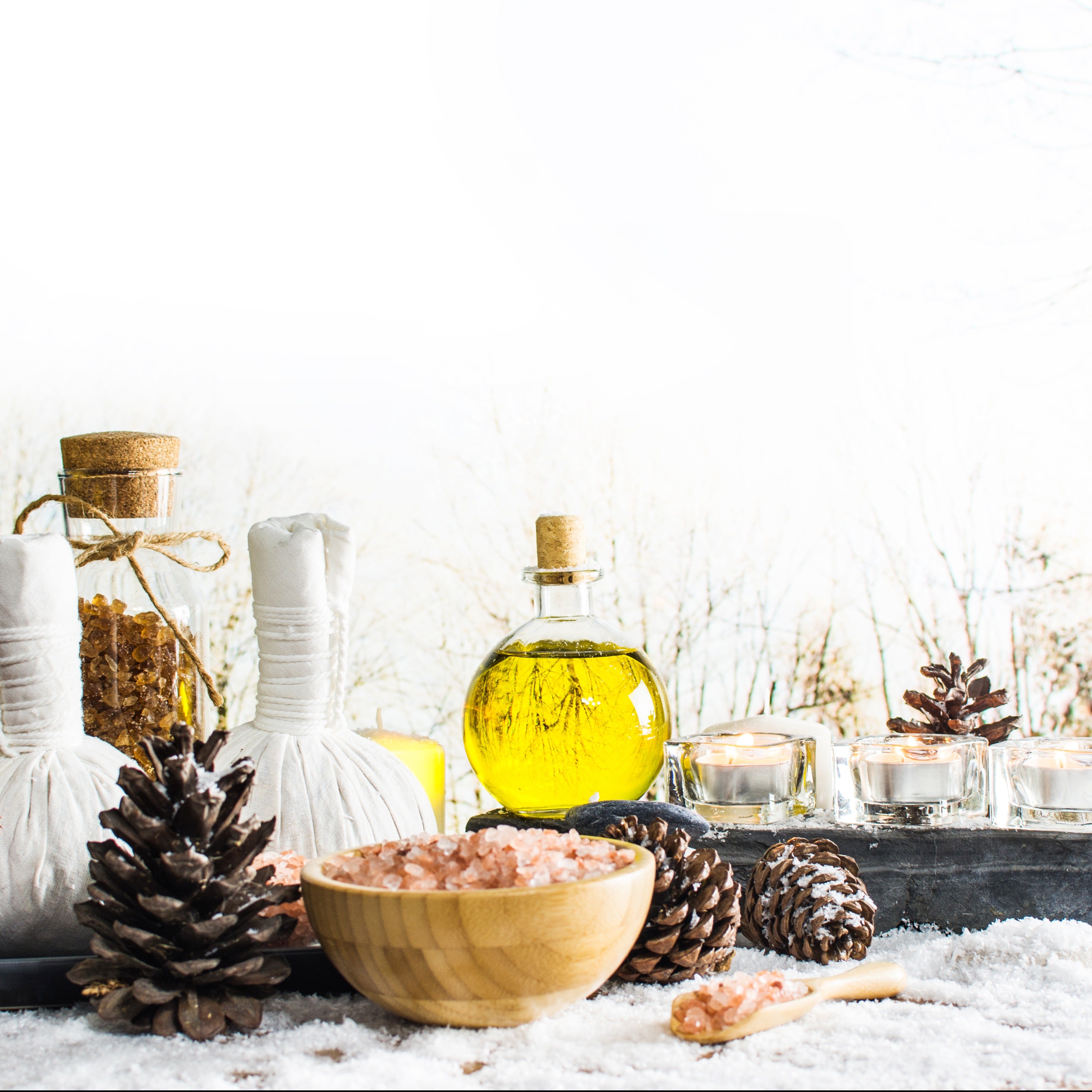 A bowl of Amber Meditation Scented Jar Candles (13 oz) from the Winter Wellness Collection by Tuscany Candle and other items on a snowy table, creating a peaceful reflection.