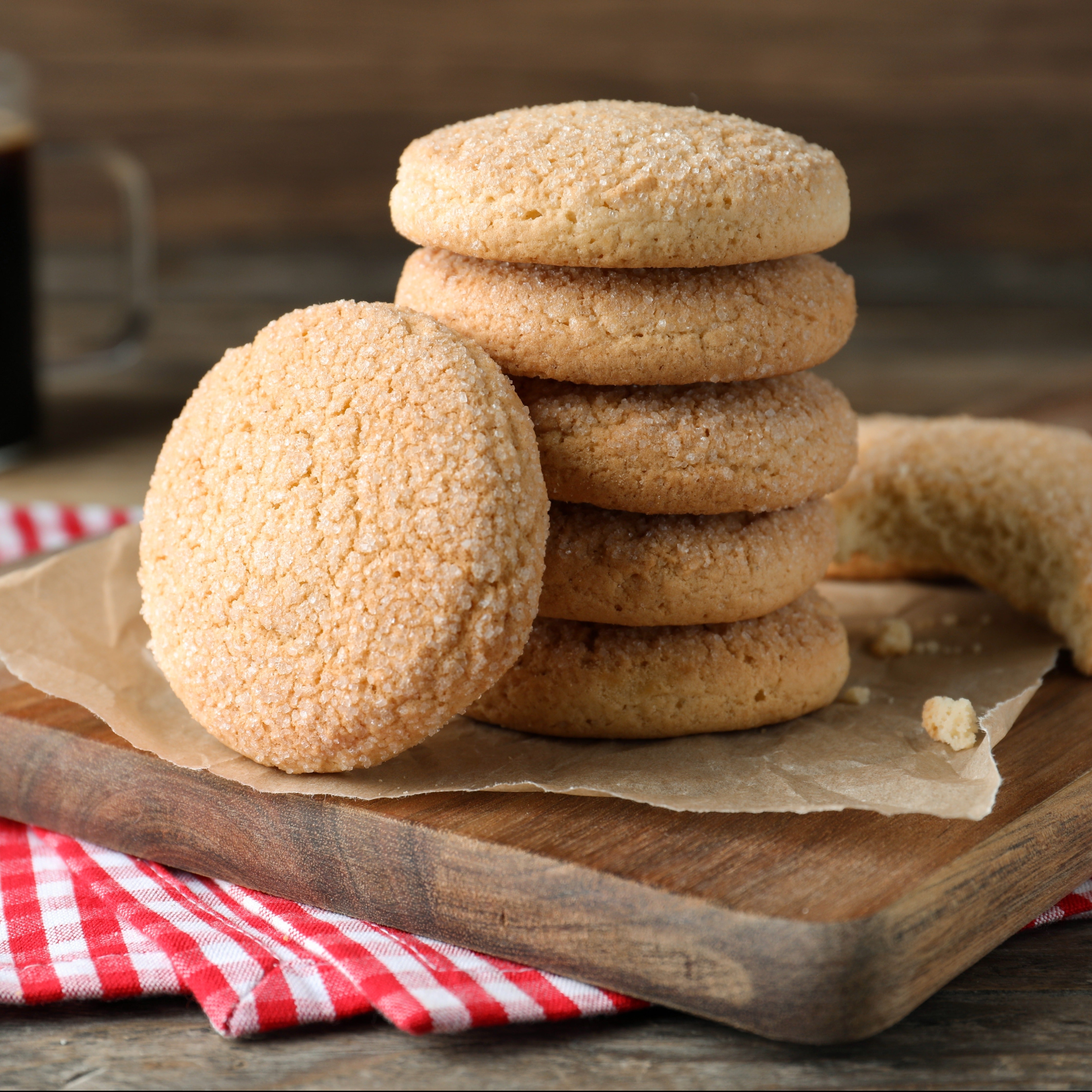 A stack of Grandma's Sugar Cookies scented wax melts (2.5 oz) on a cutting board next to a cup of coffee, accompanied by the aroma of Tuscany Candle® scented candle fragrance notes.