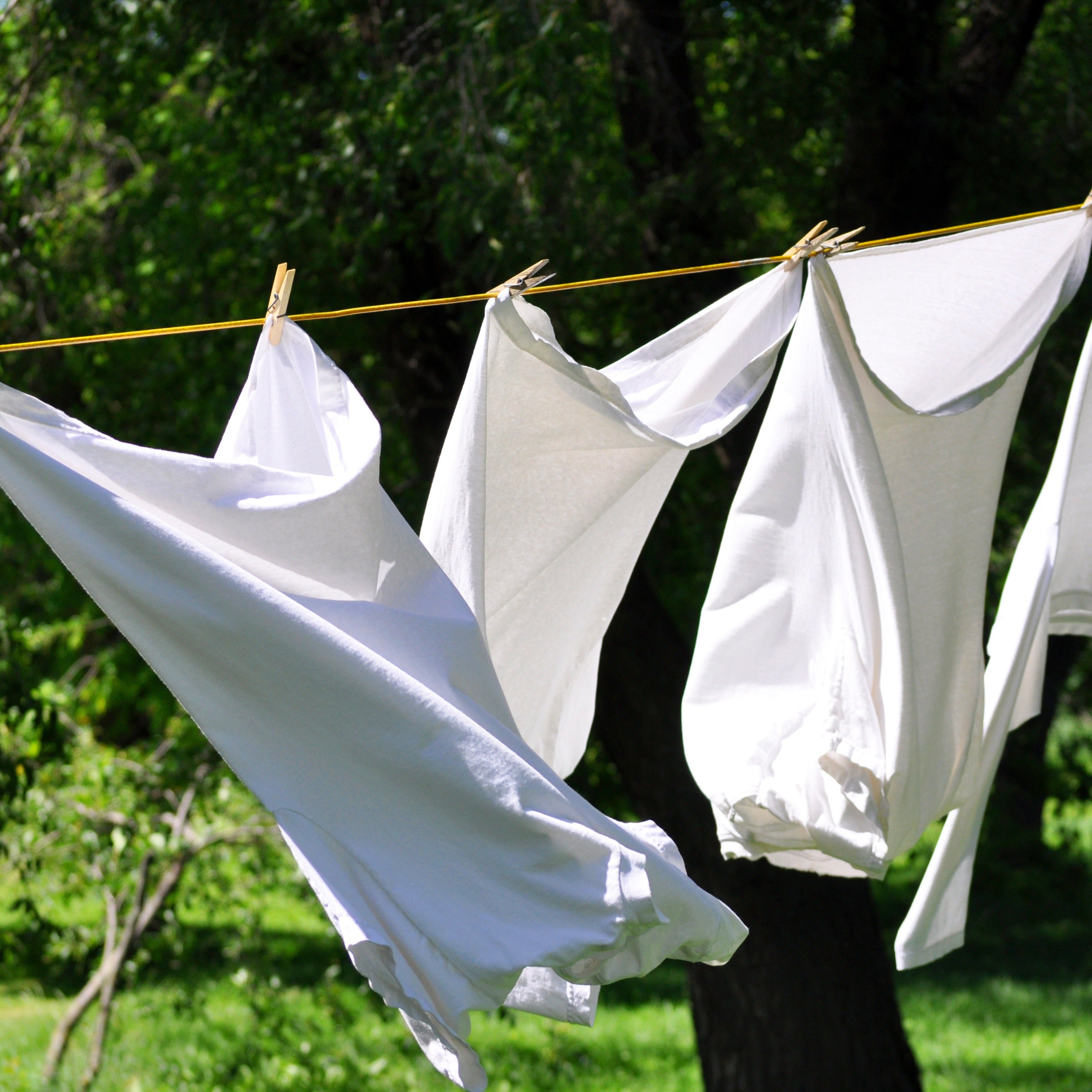 White clothes hanging on a clothesline, gently swaying in the breeze while exuding the refreshing fragrance of Tuscany Candle®'s Sunwashed Cotton Scented Wax Melt (2.5 oz).