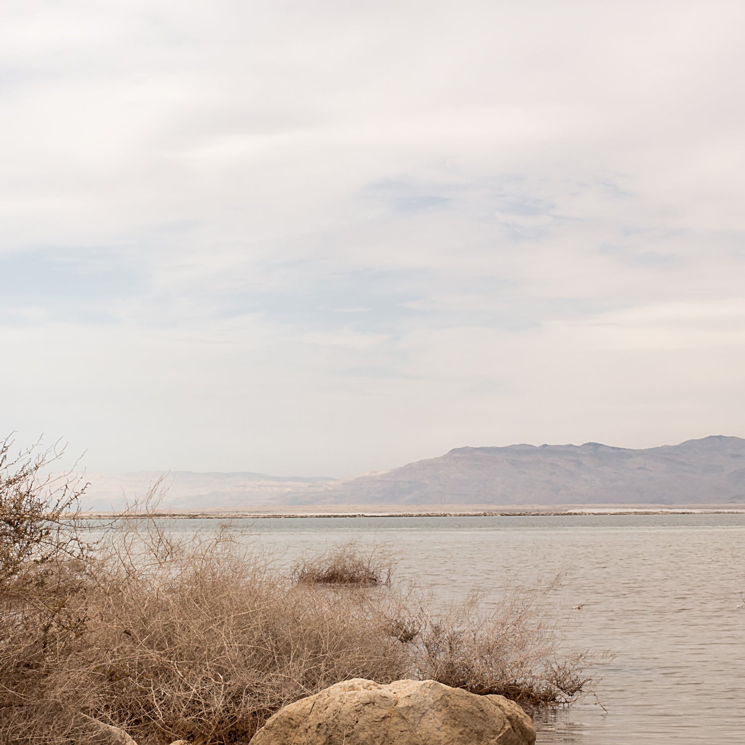 A man is sitting on a rock by the sea, enjoying the ozone-filled air and gentle fragrance notes of Tuscany Candle's Vanilla Sea Salt Long-Lasting Scented Jar Candle (14 oz).