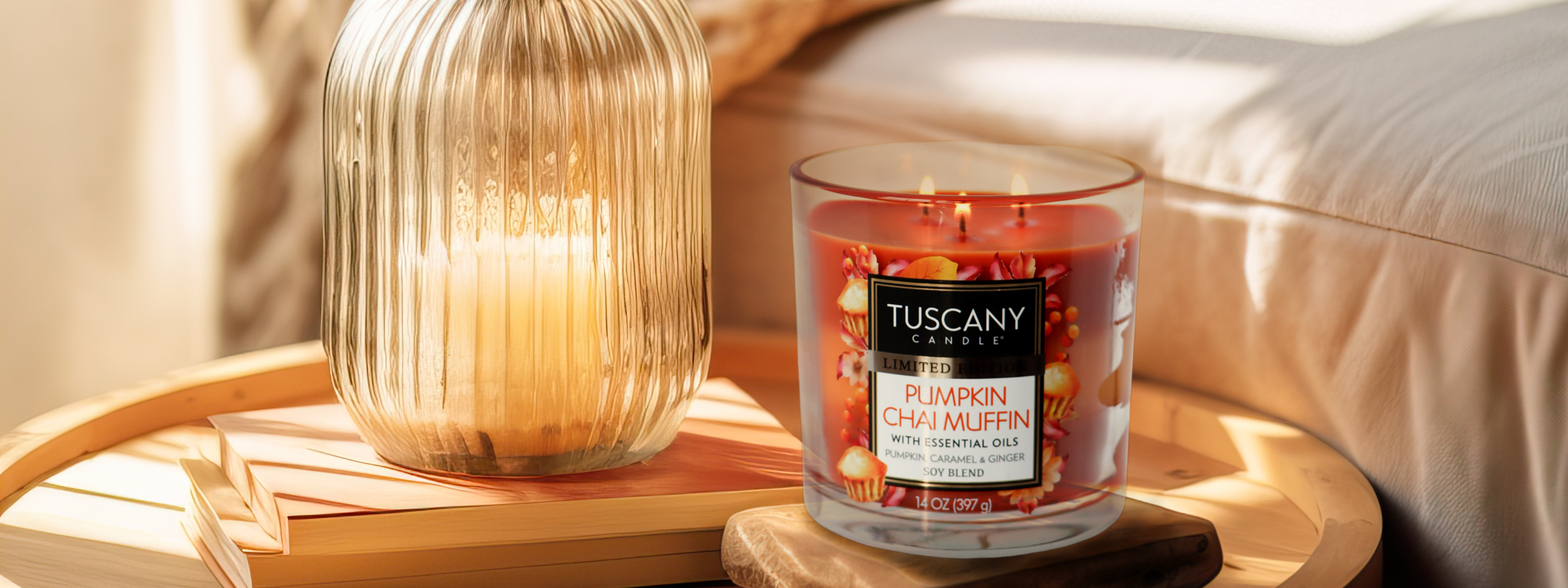 A candle labeled "Happy Harvest," with a scent of "Warm Pumpkin Pecan," is placed on a table beside a woven basket filled with orange flowers and autumn-themed foliage decor.