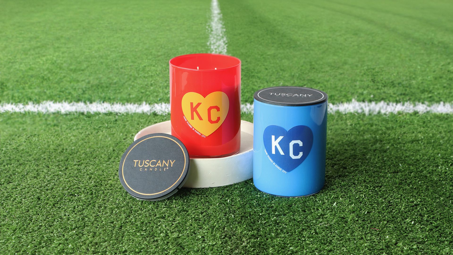 Five Tuscany Candle jars in different scents—Café Au Lait, Tobacco Leather, Evening Fireside, Citrus Peppercorn, and Tea Tree & Sandalwood—are displayed on a wooden surface.