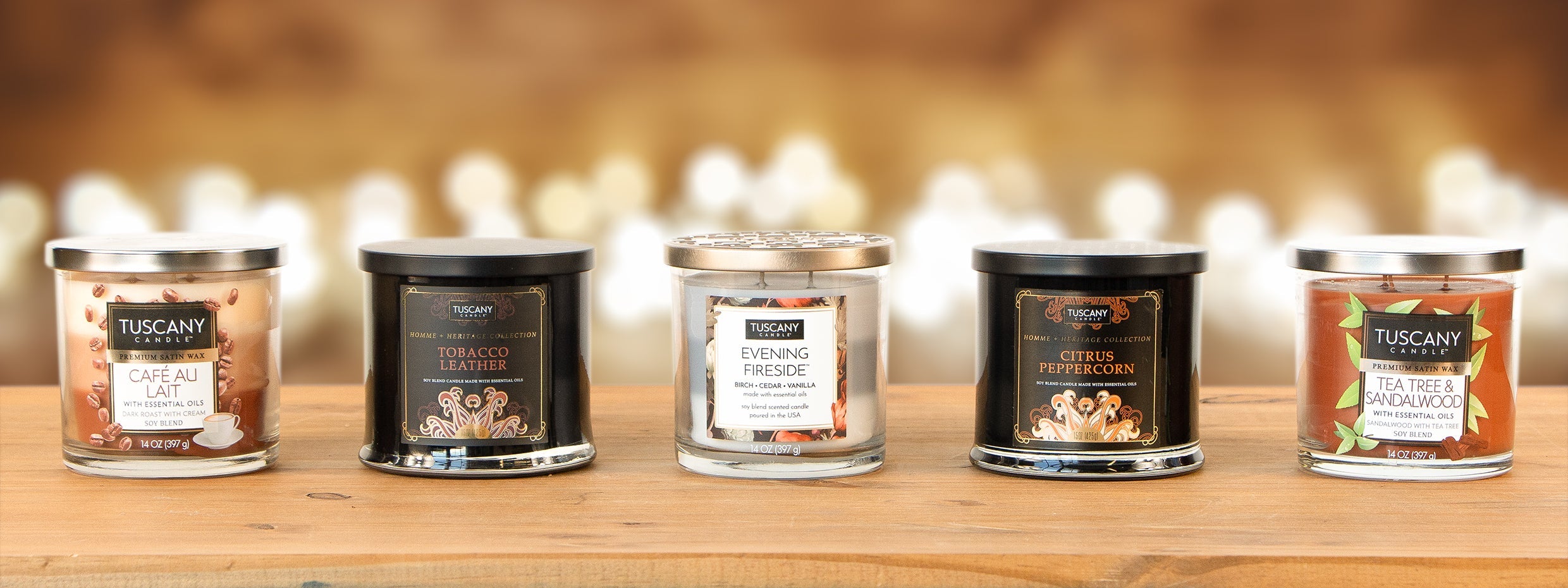 Five Tuscany Candle jars in different scents are displayed in a row on a wooden surface with a blurred background of warm lights.