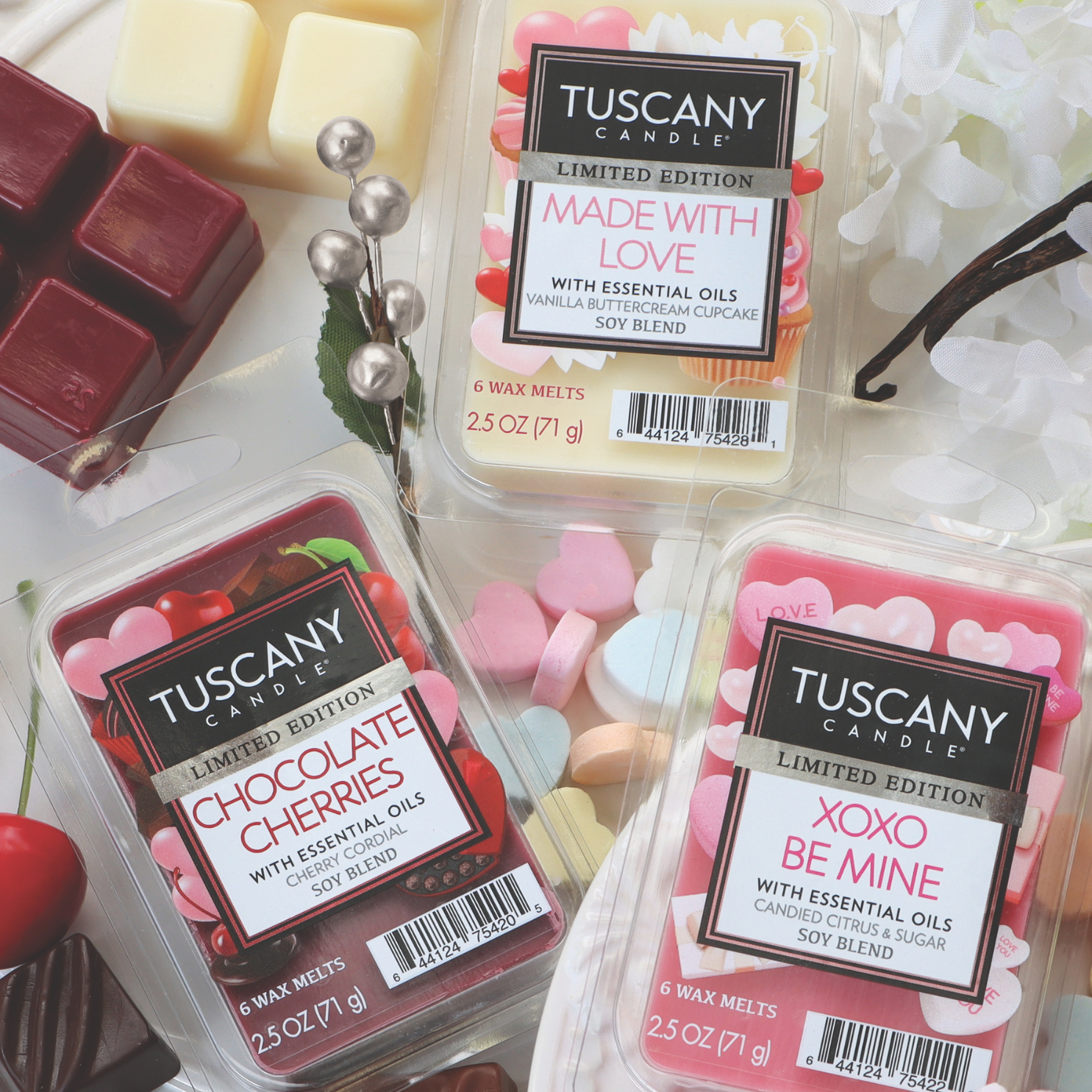 Three packs of Tuscany Candle® SEASONAL scented wax melts, featuring "Made with Love," "Chocolate Cherries," and the "XOXO Be Mine: Citrus Scented Wax Melt for Valentine’s Day (2.5 oz)," surrounded by decorative candles and flowers, create the perfect romantic atmosphere in any space.