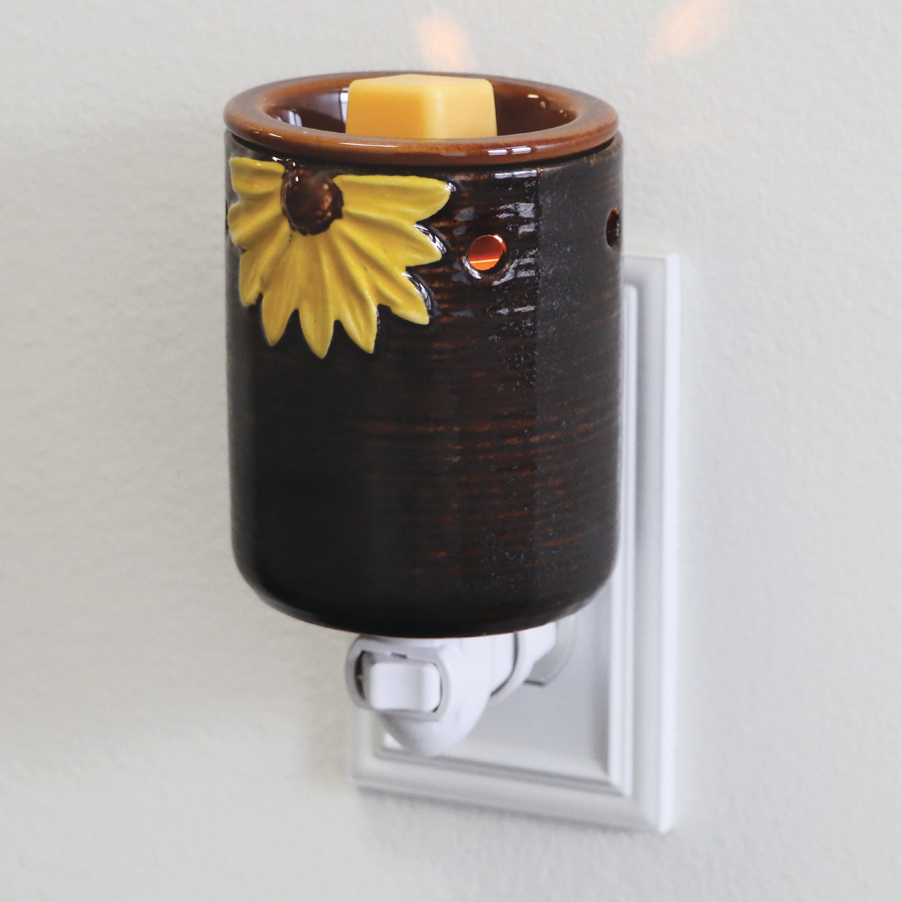 A **Sunflower Outlet Wax Melt Warmer** by **Tuscany Candle® SEASONAL** with a brown ceramic holder adorned with a yellow sunflower design and a yellow Tuscany Candle® SEASONAL wax melt inside.