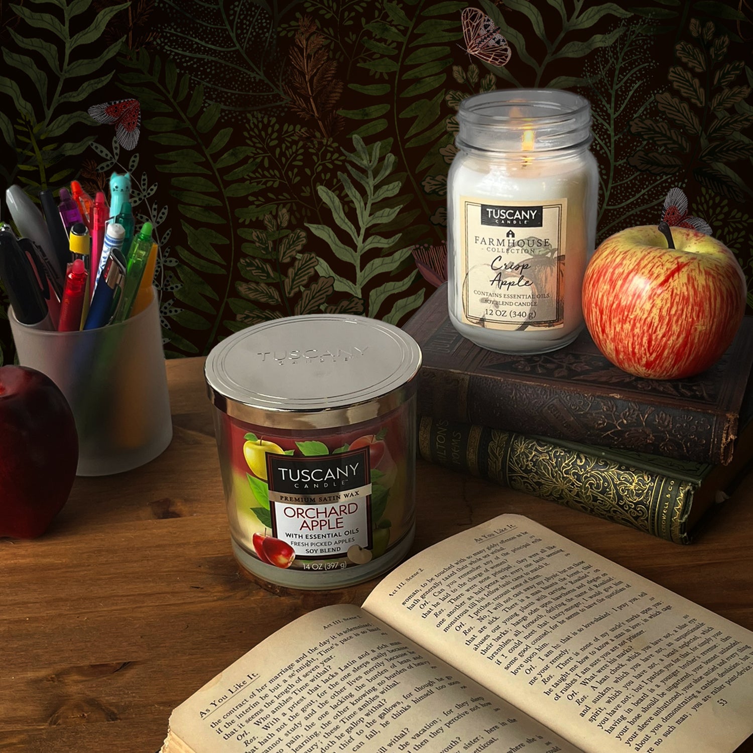 A Crisp Apple Scented Jar Candle (12 oz) from the Farmhouse Collection by Tuscany Candle® EVD sits on a table next to a book, radiating a soothing aroma.