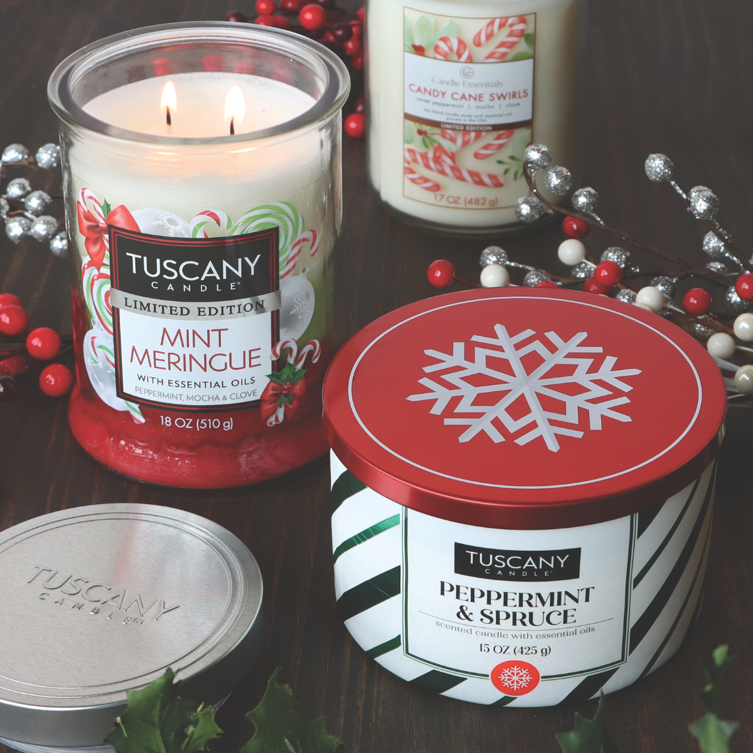 Candles branded as Tuscany Candle® SEASONAL, featuring the "Mint Meringue Long-Lasting Scented Jar Candle (18 oz)" and "Peppermint & Spruce", are displayed with festive designs including pinecones and berries on a dark wood surface.