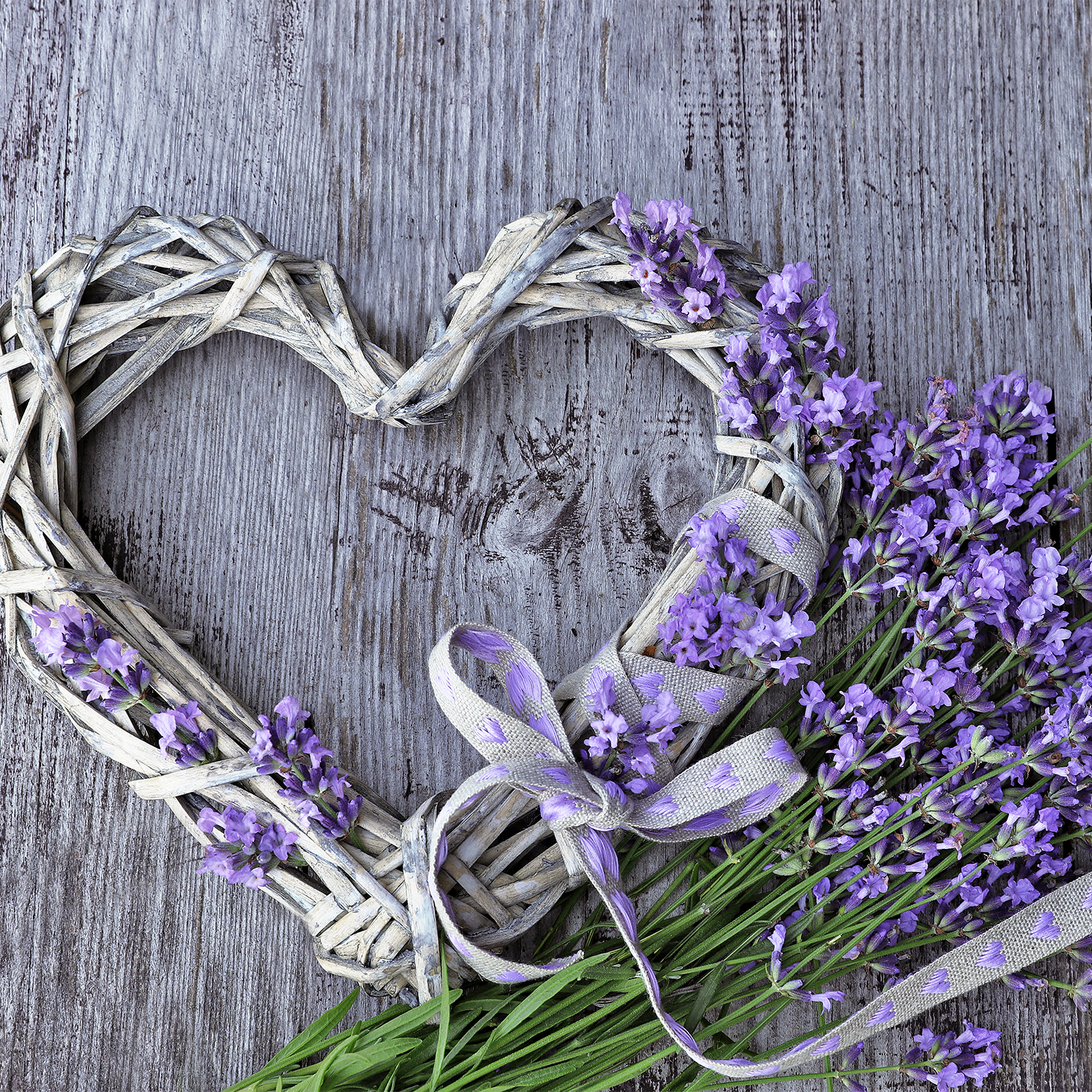 A heart-shaped arrangement of lavender flowers on a wooden table, perfect for the Love is Love Scented Ceramic Candle (10 oz) – Pride Collection by Tuscany Candle® SEASONAL.