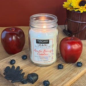 A still life photo of a scented candle from Tuscany Candle's "Farmhouse Collection", which are rustic candles packed in mason jars with black lids. The candle shown here is called "Apple Berry Cobbler"