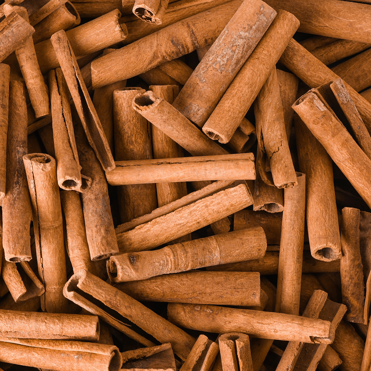 A close-up of numerous cinnamon sticks piled together, displaying their brown hues and rough textures, evokes the autumnal aromas reminiscent of a Tuscany Candle® SEASONAL Spooky Pumpkin Spice Long-Lasting Scented Jar Candle (12 oz).