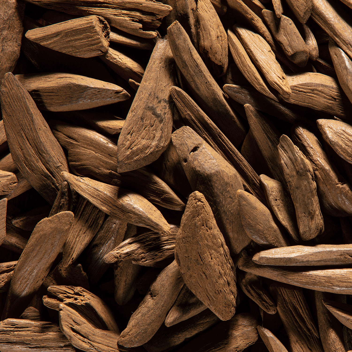 A close-up view of a pile of wooden mulch chips, showcasing various sizes and shapes of the brown, splintered pieces, perfect for surrounding gardenia plants or complementing the Midnight Broomstick Rides Long-Lasting Scented Jar Candle (12 oz) by Tuscany Candle® SEASONAL.