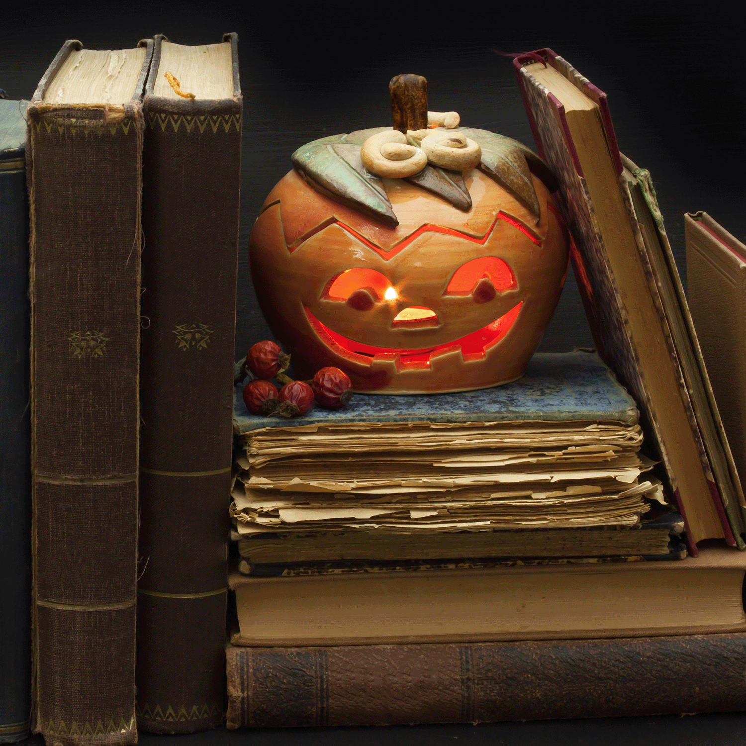 The Book Of Spells Long-Lasting Scented Jar Candle by Tuscany Candle® SEASONAL sits atop a stack of aged books, surrounded by more old books, creating the perfect Halloween ambiance.