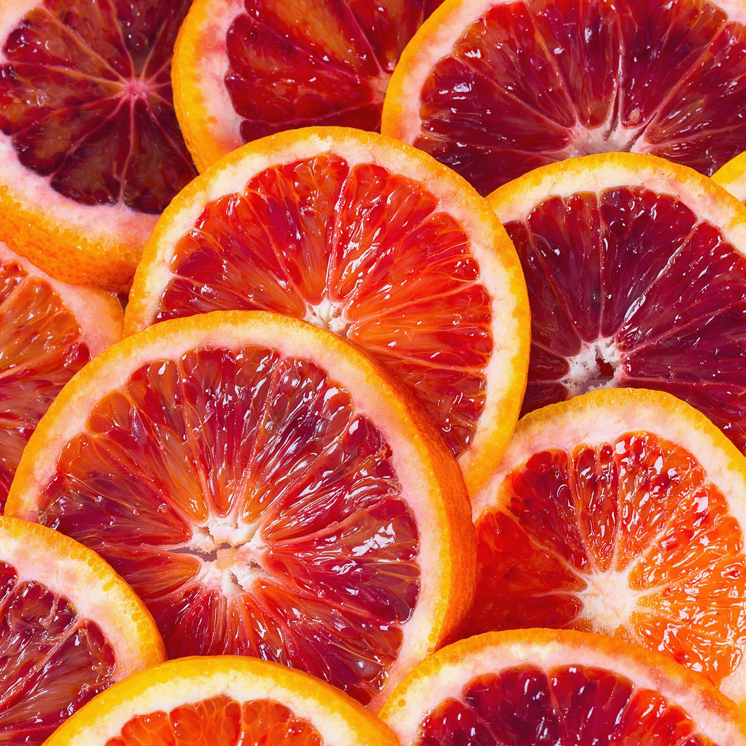 A close-up of multiple overlapped slices of blood oranges reveals their vibrant red and orange hues, ideal for evoking Halloween festivities. Pair them with an Enchanted Witches Brew Long-Lasting Scented Jar Candle (12 oz) by Tuscany Candle® SEASONAL to create a perfectly festive atmosphere.