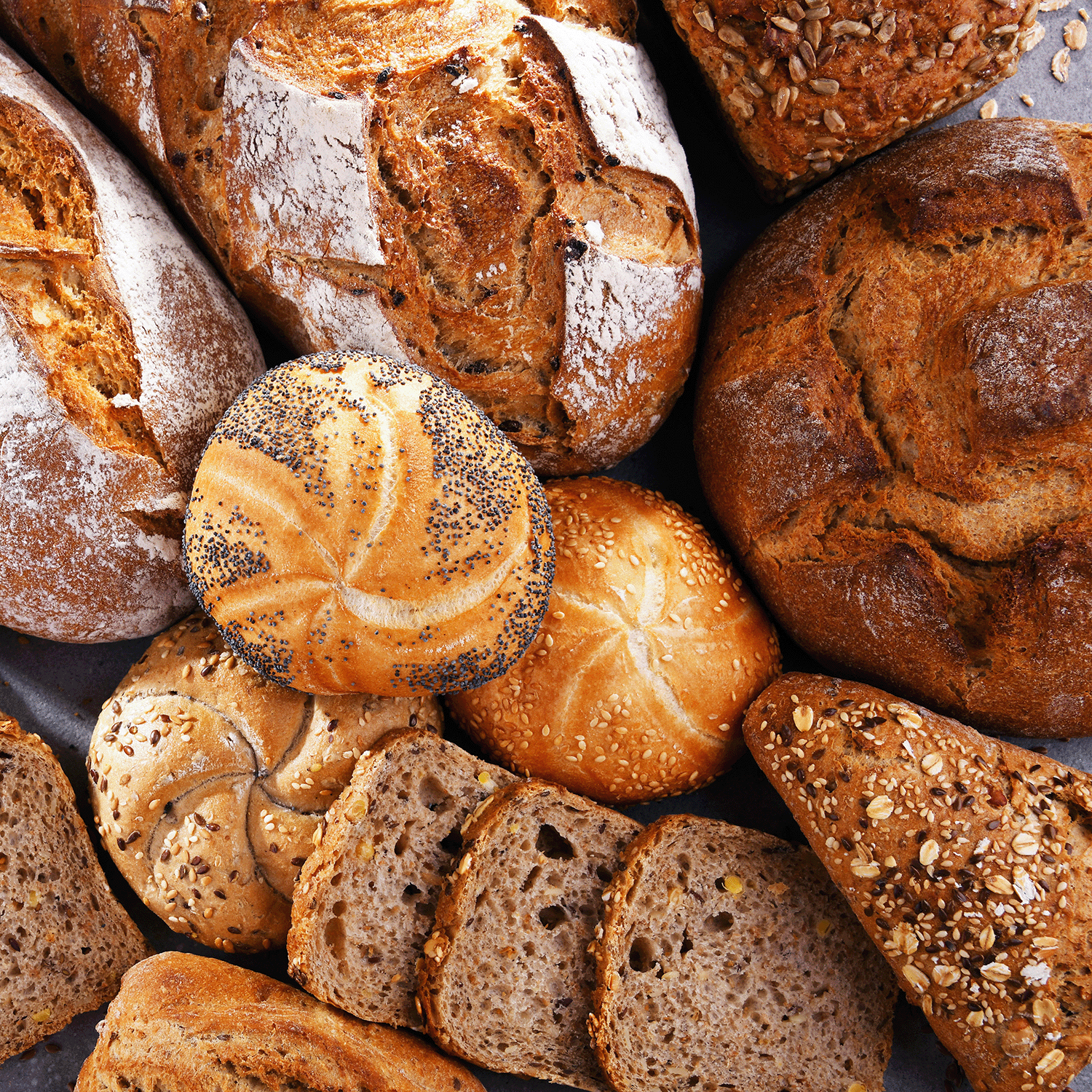 Various types of bread, including loaves, rolls, and slices topped with seeds and grains, displayed in a close-up arrangement. The cozy and festive setup perfectly complements the essence of autumn with the warm aroma from the Pumpkin Spice Everything Long-Lasting Scented Jar Candle (12 oz) from Tuscany Candle® SEASONAL's Autumn Flannels Collection.