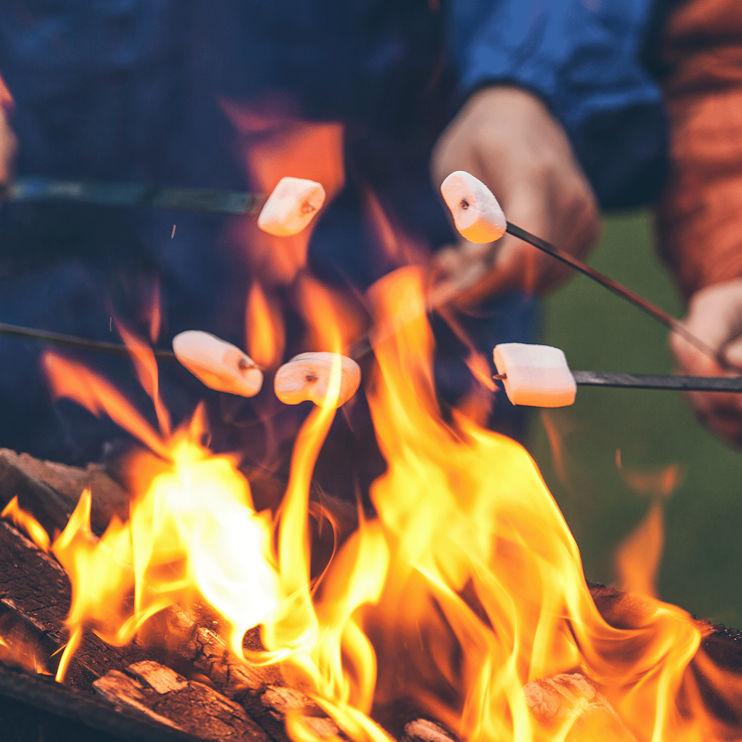 People enjoying the relaxing aroma of Cozy Fireside Marshmallows Long-Lasting Scented Jar Candle (12 oz) from the Autumn Flannels Collection by Tuscany Candle® SEASONAL. The flames are visible, creating a cozy atmosphere similar to roasting marshmallows over a campfire.