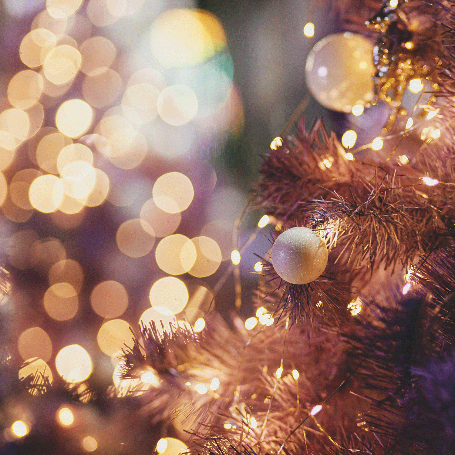 Close-up of a decorated Christmas tree with glowing lights and ornaments, enhanced by the Mulberry Bliss Long-Lasting Scented Jar Candle (18 oz) from Tuscany Candle® SEASONAL. Blurred lights in the background create a stunning bokeh effect.