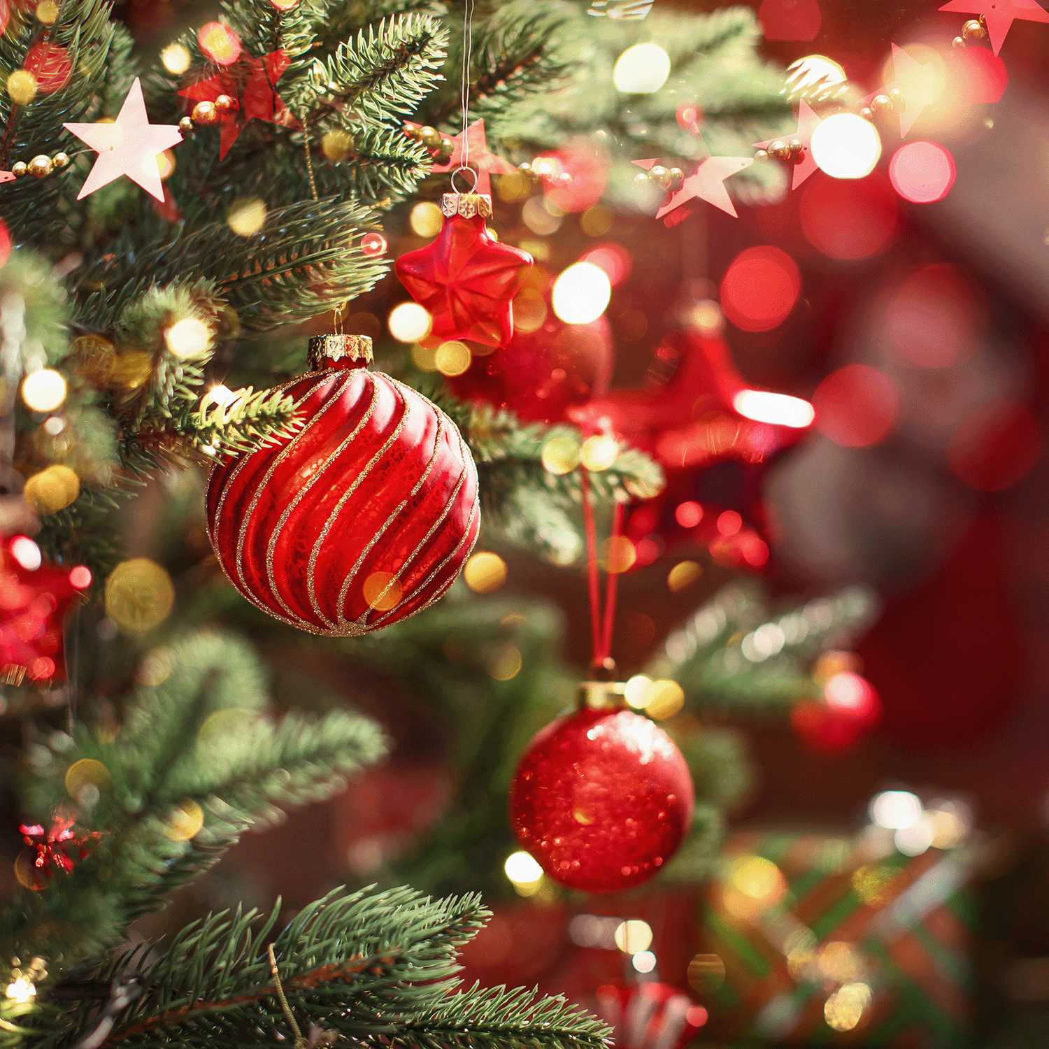 Close-up of a Christmas tree adorned with red and gold ornaments and stars, set against a backdrop of blurred festive lights, alongside the Down The Chimney Long-Lasting Scented Jar Candle (14 oz) by Tuscany Candle® SEASONAL that fills the air with its warm cedar clove pepper fragrance.