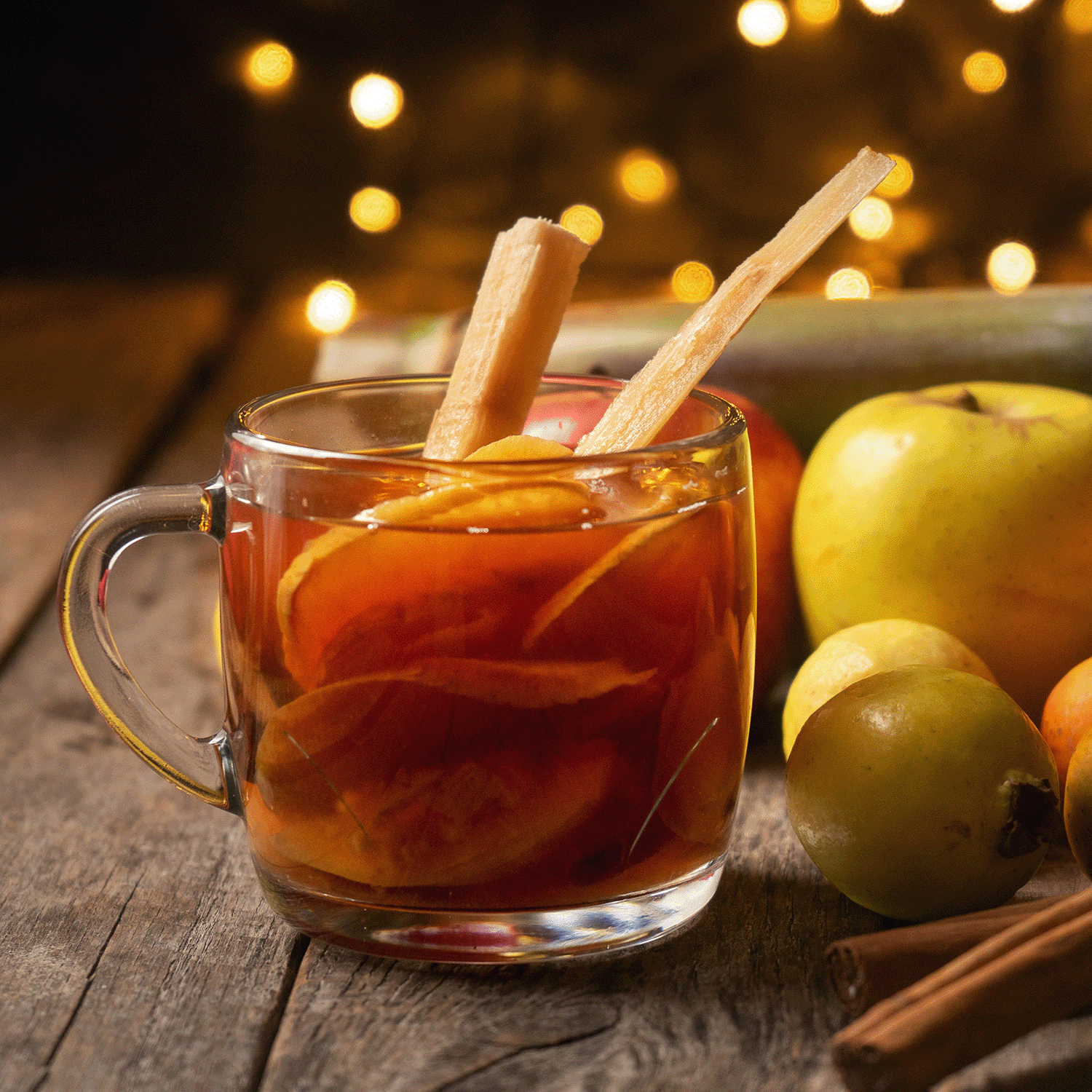 An 18 oz Tuscany Candle® SEASONAL Yuletide Cider scented jar candle sits on a wooden surface, with apples and festive lights glowing warmly in the background, perfectly capturing the holiday spirit.