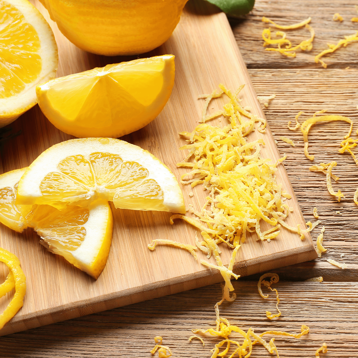 Lemon slices, zest, and a whole lemon rest on a wooden cutting board on a rustic surface, evoking the aroma of Sugared Citron: Sweet Melon Scented Spring Candle by Tuscany Candle® SEASONAL.