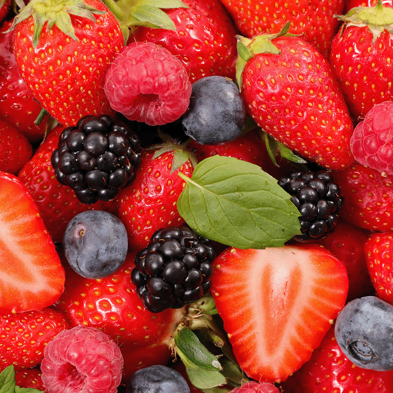 A close-up of Tuscany Candle® SEASONAL’s Tropical Vanilla: Berries & Vanilla Scented Summer Candle (14 oz), inspired by fresh strawberries, blackberries, blueberries, raspberries, and green leaves.