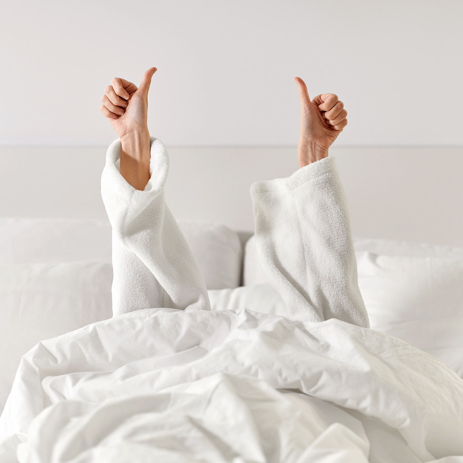 A person gives two thumbs up, relaxed in bed and wrapped in a white robe, as the gentle aroma of Tuscany Candle® SEASONAL Lime Blossom: Linen Scented Spring Wax Melt (2.5 oz) fills the room with fresh spring notes.