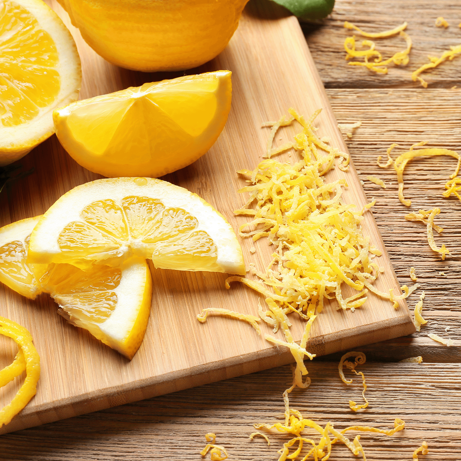 Lemon wedges and zest adorn a wooden cutting board, while the air fills with vibrant citrus notes from Sugared Citron: Sweet Melon Scented Spring Wax Melt by Tuscany Candle® SEASONAL scattering across the table.