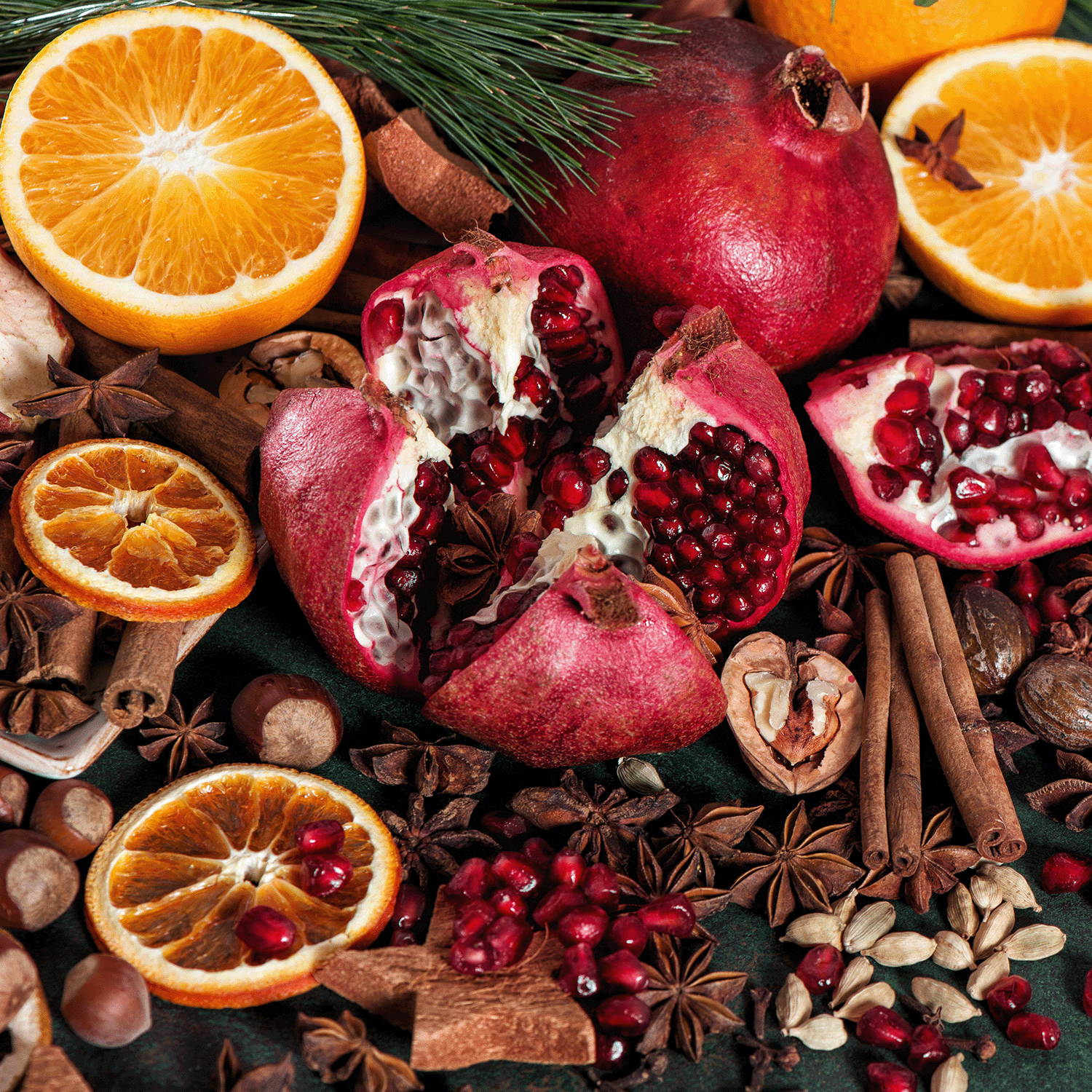 The essence of a Tuscany Candle® SEASONAL Spiced Cinnamon Scented Jar Candle from the Winter Reverie Collection (18 oz) is captured by a halved pomegranate surrounded by orange slices, pine cones, and cinnamon sticks, while star anise and assorted nuts complete this cozy holiday décor.