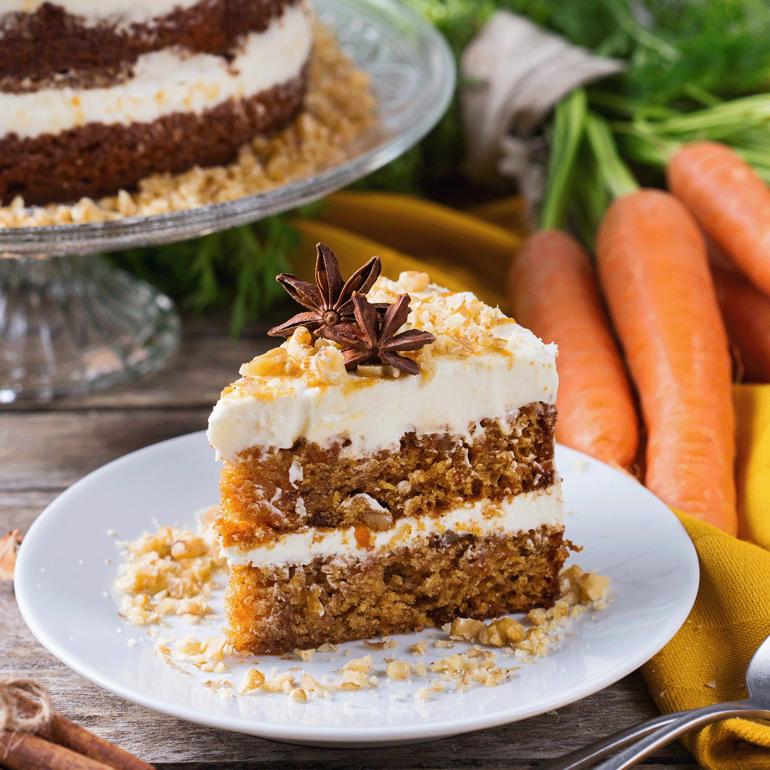 A slice of carrot cake with cream cheese frosting and nuts sits on a plate, evoking the warm aroma of Tuscany Candle® SEASONAL's Ginger Carrot Cake: Spice Cake & Sugar Scented Fall Candle (12 oz) from the Bakery Tins Collection.