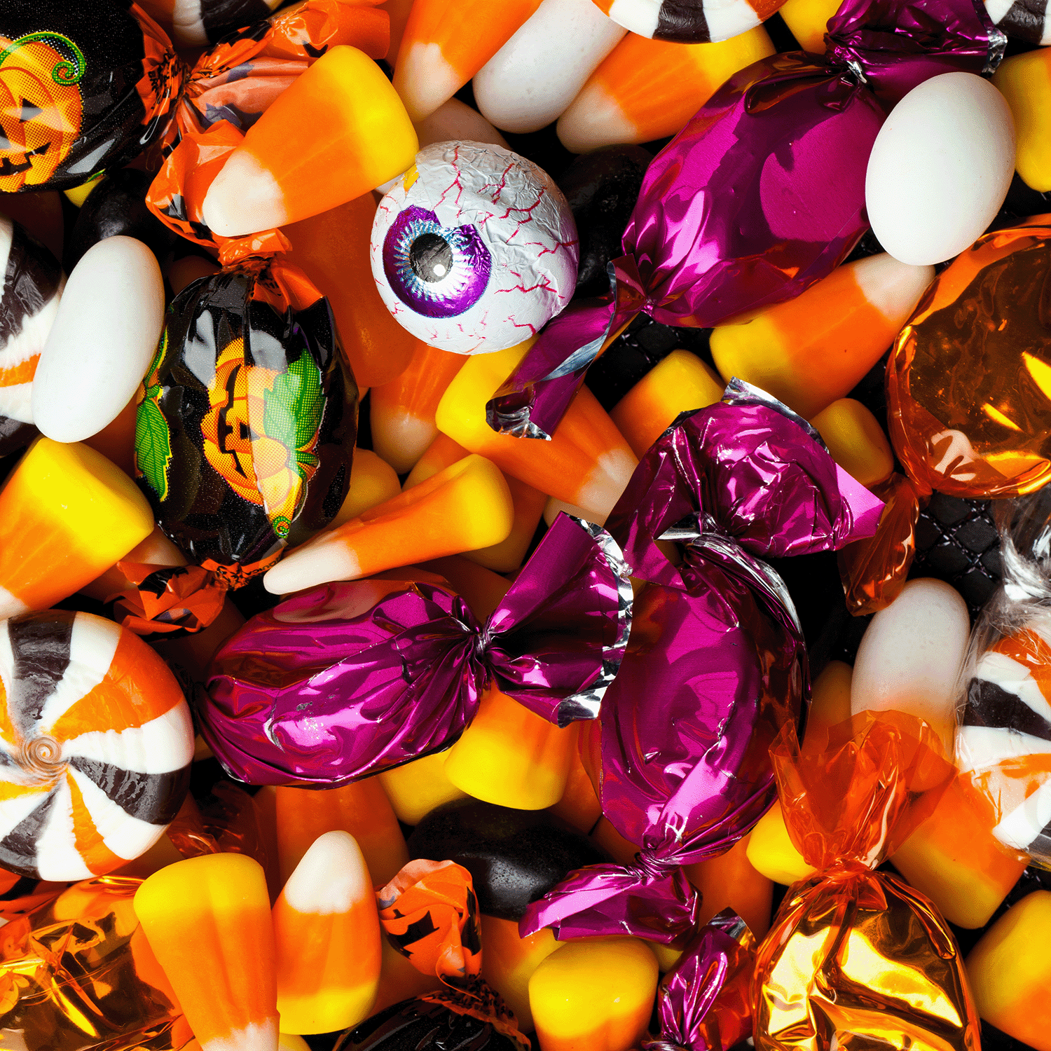 A pile of assorted Halloween candies—candy corn, chocolates, and eyeball sweets in festive colors—pairs perfectly with the Trick or Treat: Sugared Candy Corn Scented Halloween Candle (14 oz) by Tuscany Candle® SEASONAL from the Mysteriously Spooky Collection.