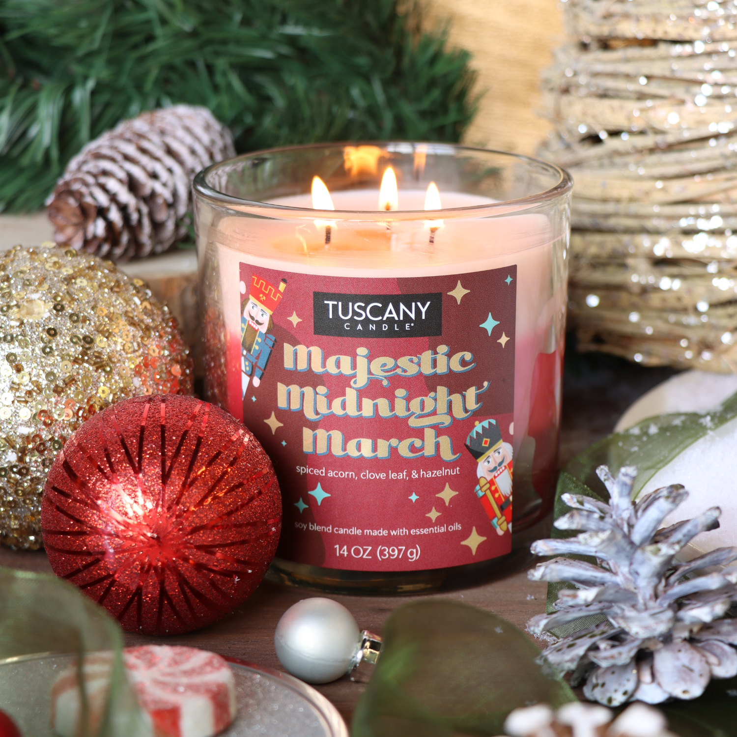 A Tuscany Candle® SEASONAL Majestic Midnight March Scented Holiday Candle (14 oz) is lit and surrounded by Christmas ornaments, pinecones, and greenery on a festive holiday background.