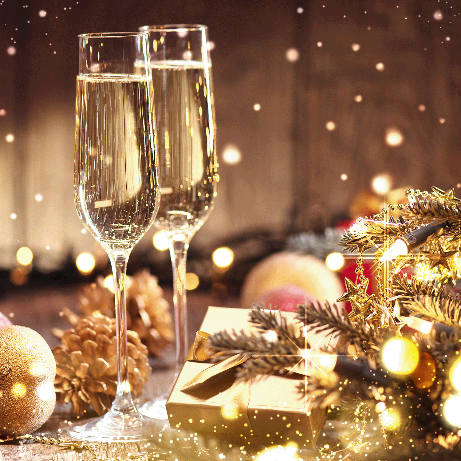 Two champagne flutes, a gold gift, pine cones, baubles, and glowing lights set a festive scene—ideal for enjoying the sparkling aroma of Tuscany Candle® SEASONAL Mimosas & Cheer: Champagne & Yuzu Scented Holiday Wax Melt (2.5 oz).