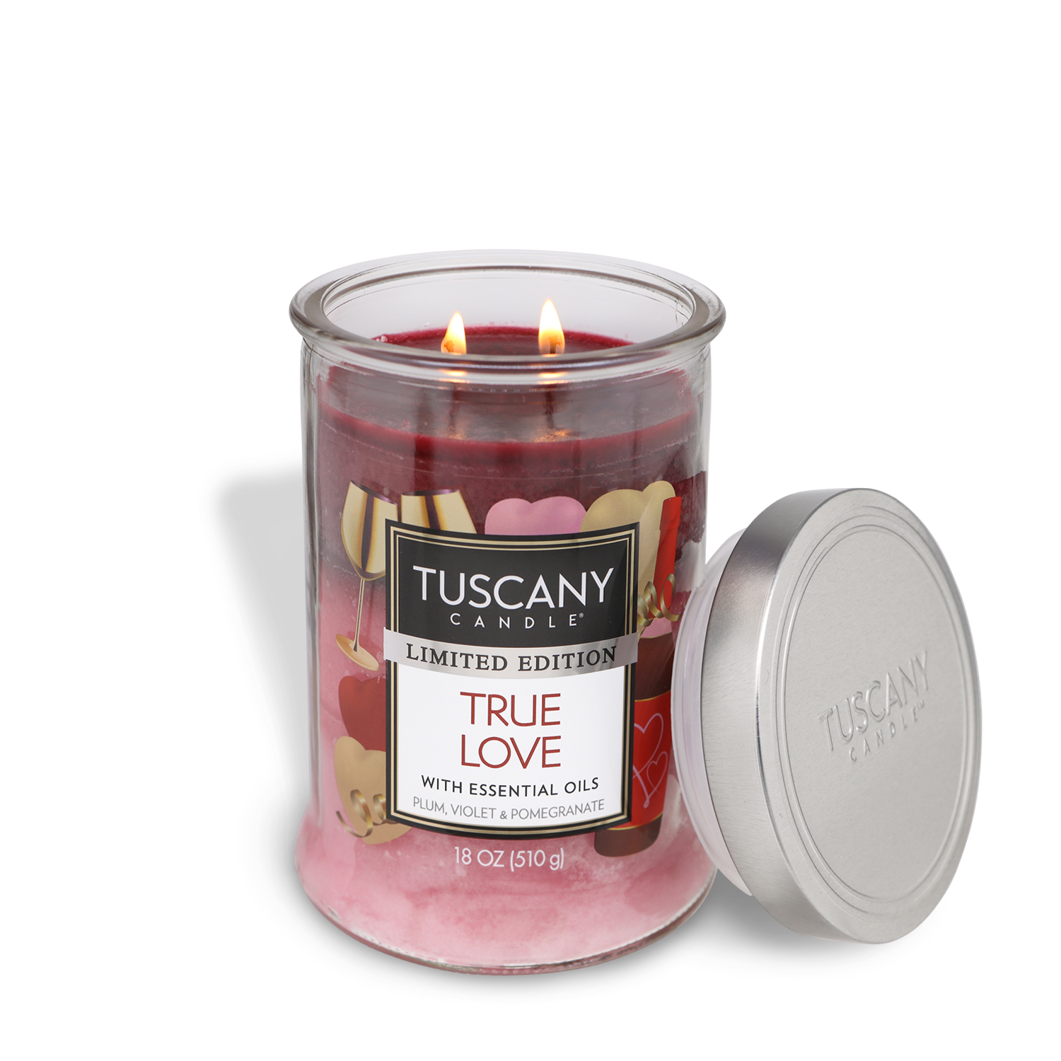 An 18 oz glass jar candle labeled "True Love: Plum & Pomegranate" by Tuscany Candle® SEASONAL, featuring heart decorations, two lit wicks, and a silver lid set to the side.