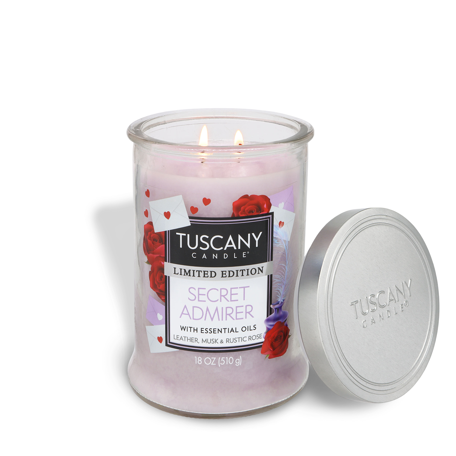An 18 oz Tuscany Candle® SEASONAL "Secret Admirer: Leather & Musk Scented Valentine's Candle" in a glass jar with two lit wicks, rose and envelope label details, and the silver lid set aside.