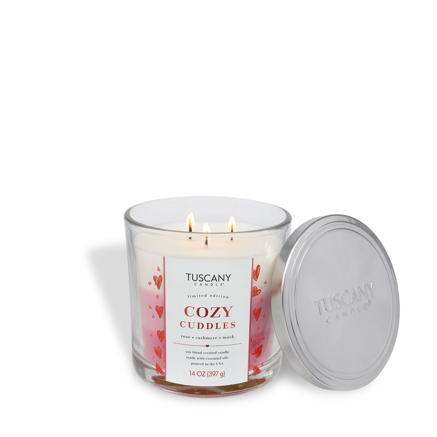 A Tuscany Candle® SEASONAL Cozy Cuddles: Rose & Cashmere Scented Valentine's Candle (14 oz) with three lit wicks in a glass jar, silver lid on the side, and a label decorated with red hearts.