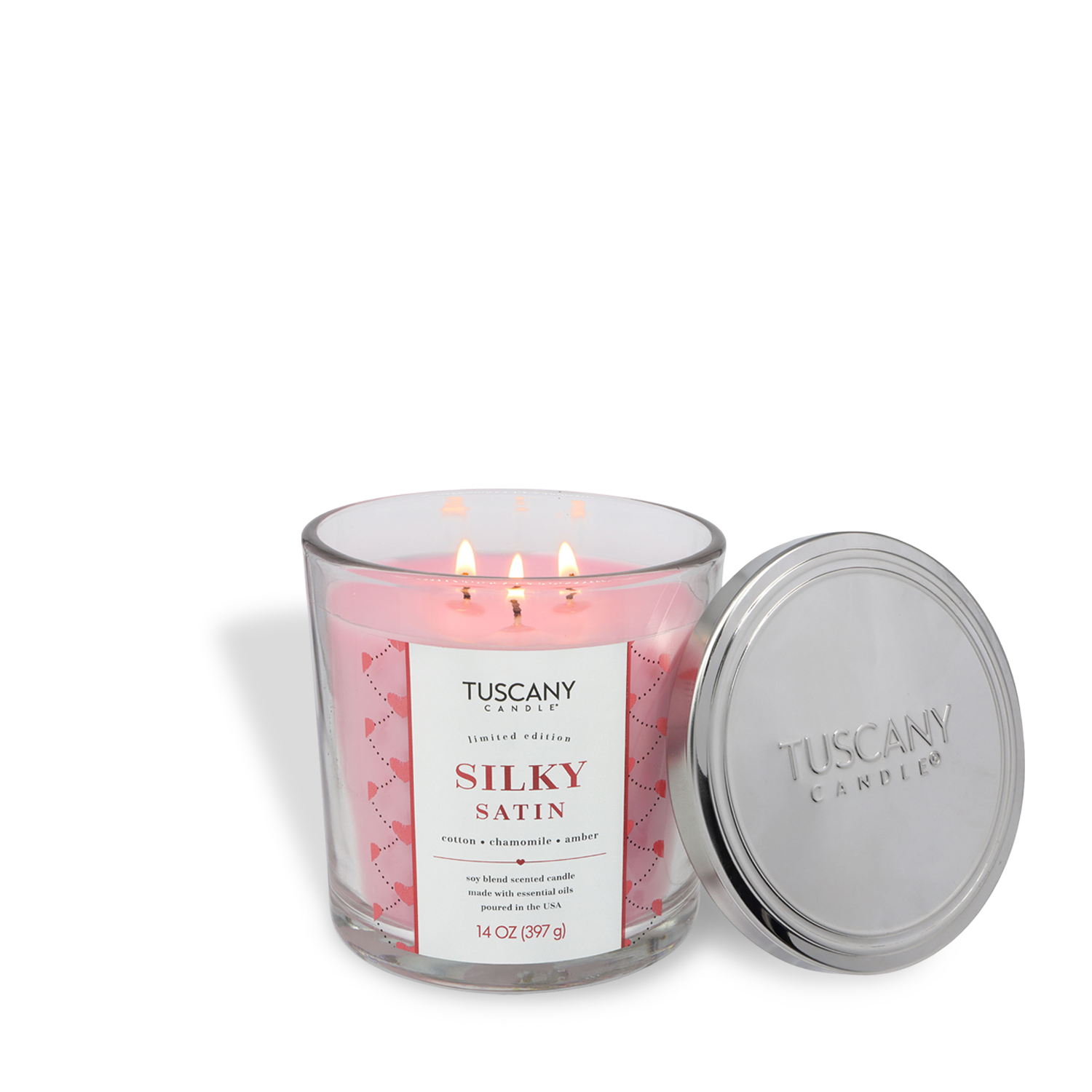 A pink Tuscany Candle® SEASONAL "Silky Satin: Cotton & Chamomile" Valentine's Candle (14 oz) with cotton, chamomile, and amber scents sits in a clear glass jar with its silver lid beside it.