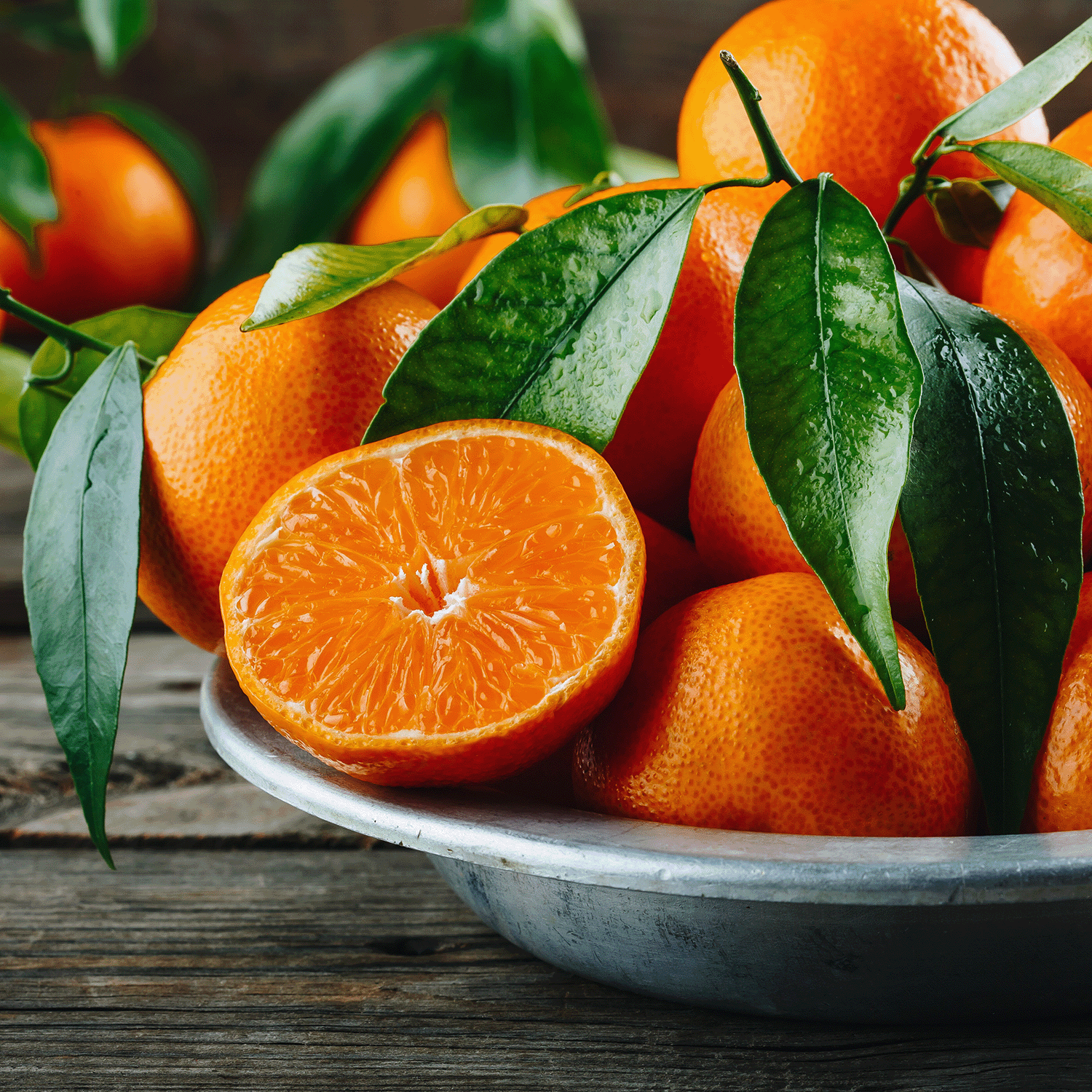 A XOXO: Yuzu & Champagne Scented Valentine's Candle (12 oz) by Tuscany Candle® SEASONAL sits on a wooden surface, surrounded by fresh tangerines with green leaves and one tangerine sliced in half.