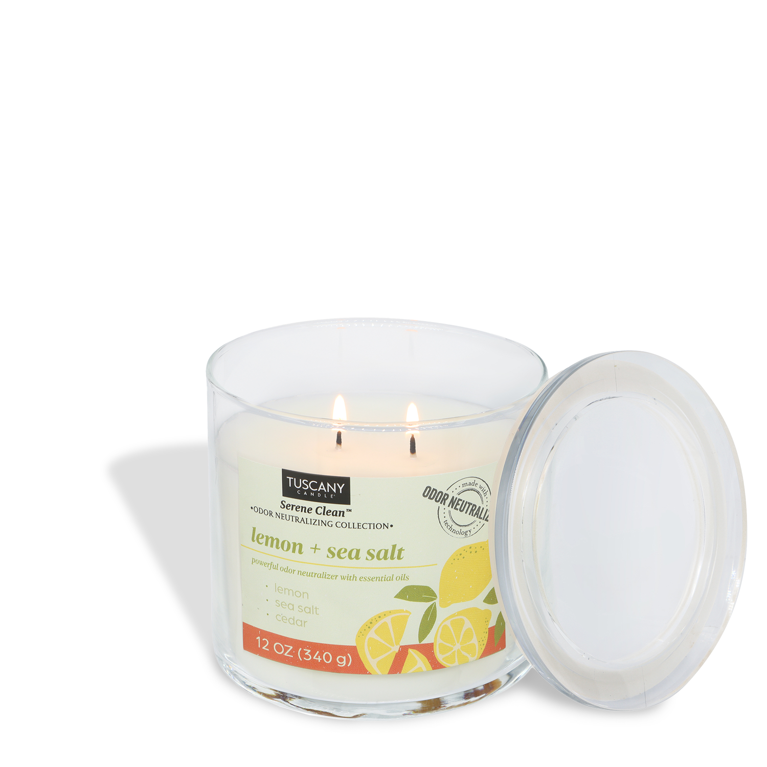 A lit Tuscany Candle® Everyday Lemon + Seasalt Scented Odor Neutralizing Candle (12 oz) from the Serene Clean Collection sits in a clear glass jar with its lid nearby. The label displays lemon and sea salt illustrations.