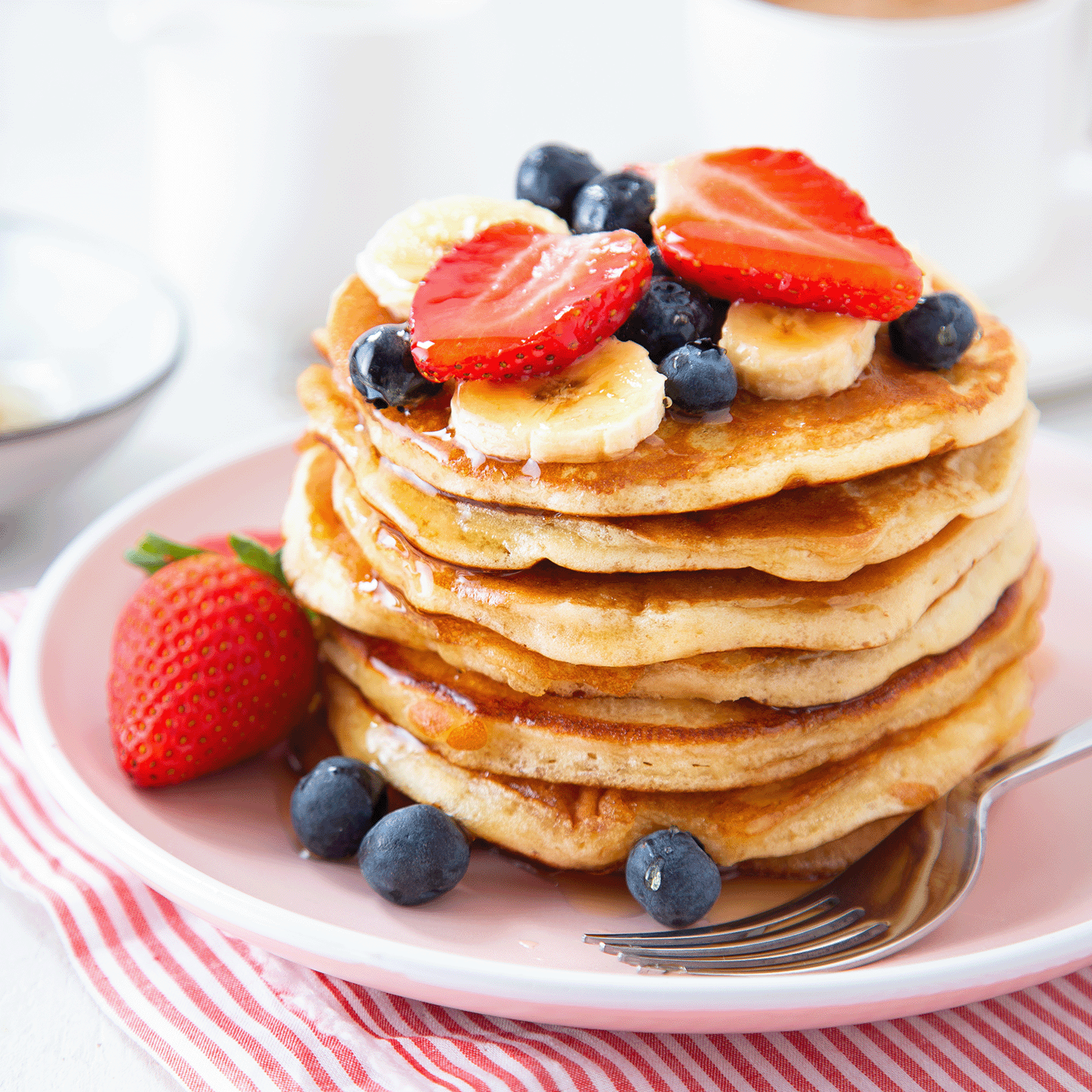 A stack of maple butter pancakes with strawberries, blueberries, and bananas sits on a pink plate, evoking the cozy scent of Tuscany Candle® SEASONAL Sunday Morning: Maple Butter Pancakes Scented Spring Wax Melt (2.5 oz).