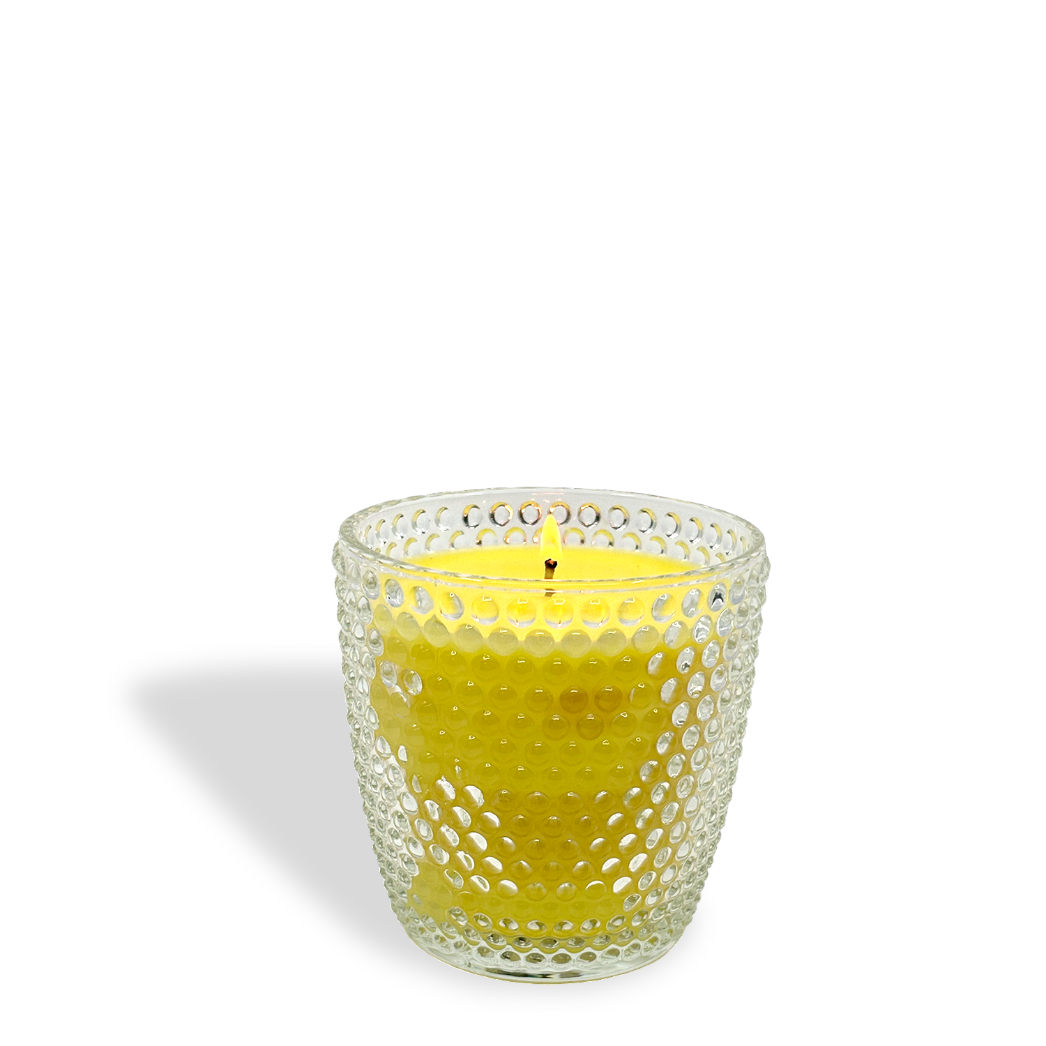 The Blooming Daffodils: Orange & Hibiscus Scented Easter Candle (8.5 oz) by Tuscany Candle® sits in a clear, textured dotted glass holder, its yellow wax casting a shadow on a white background.