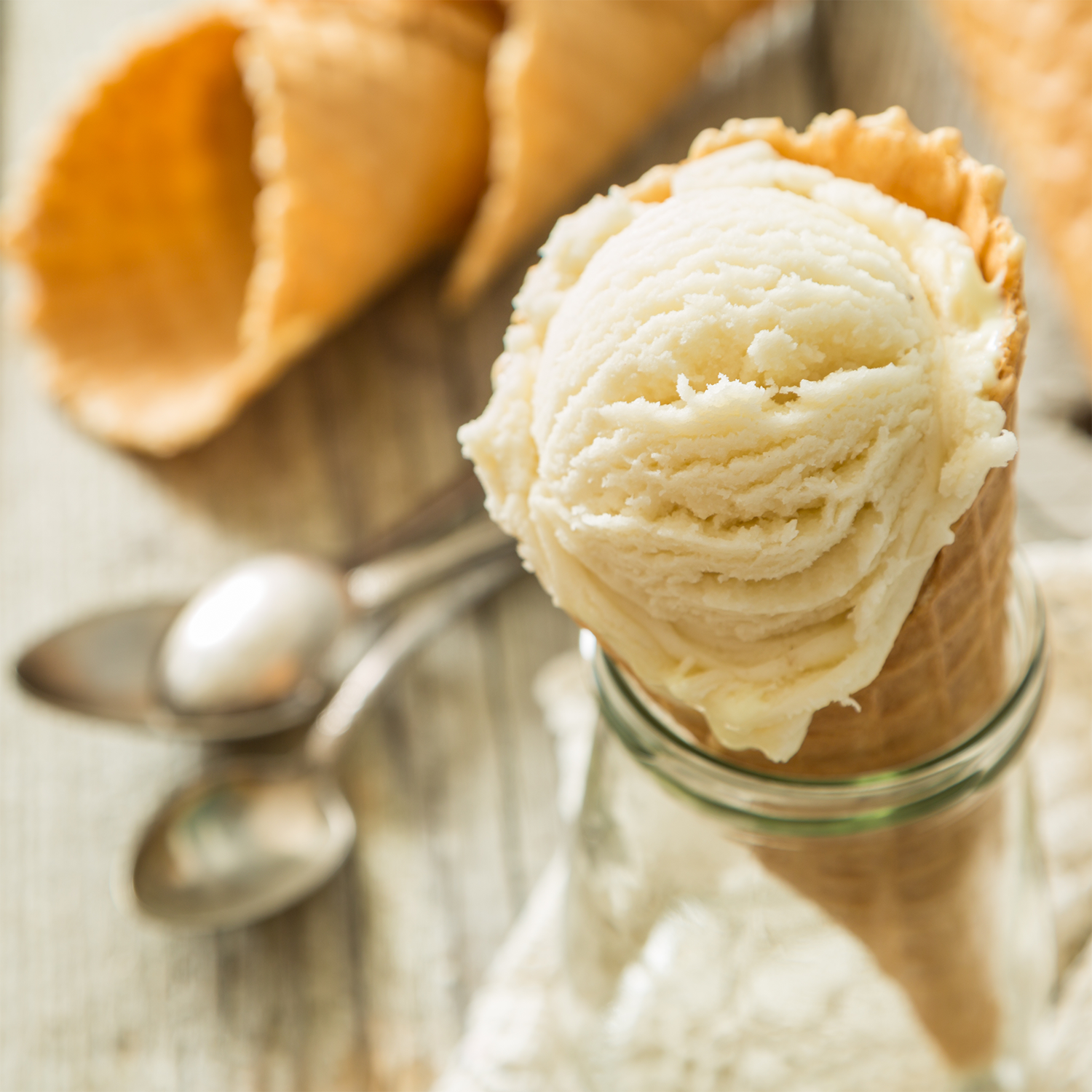 A scoop of vanilla ice cream in a waffle cone with two spoons pairs perfectly with the fresh aroma of Tuscany Candle® SEASONAL Tangerine Cream Pop: Orange & Vanilla Scented Spring Candle (14 oz) for a delightful spring home fragrance.